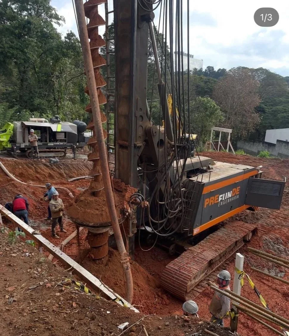 Máquina de perfuração de solo em um canteiro de obras, com trabalhadores ao redor.