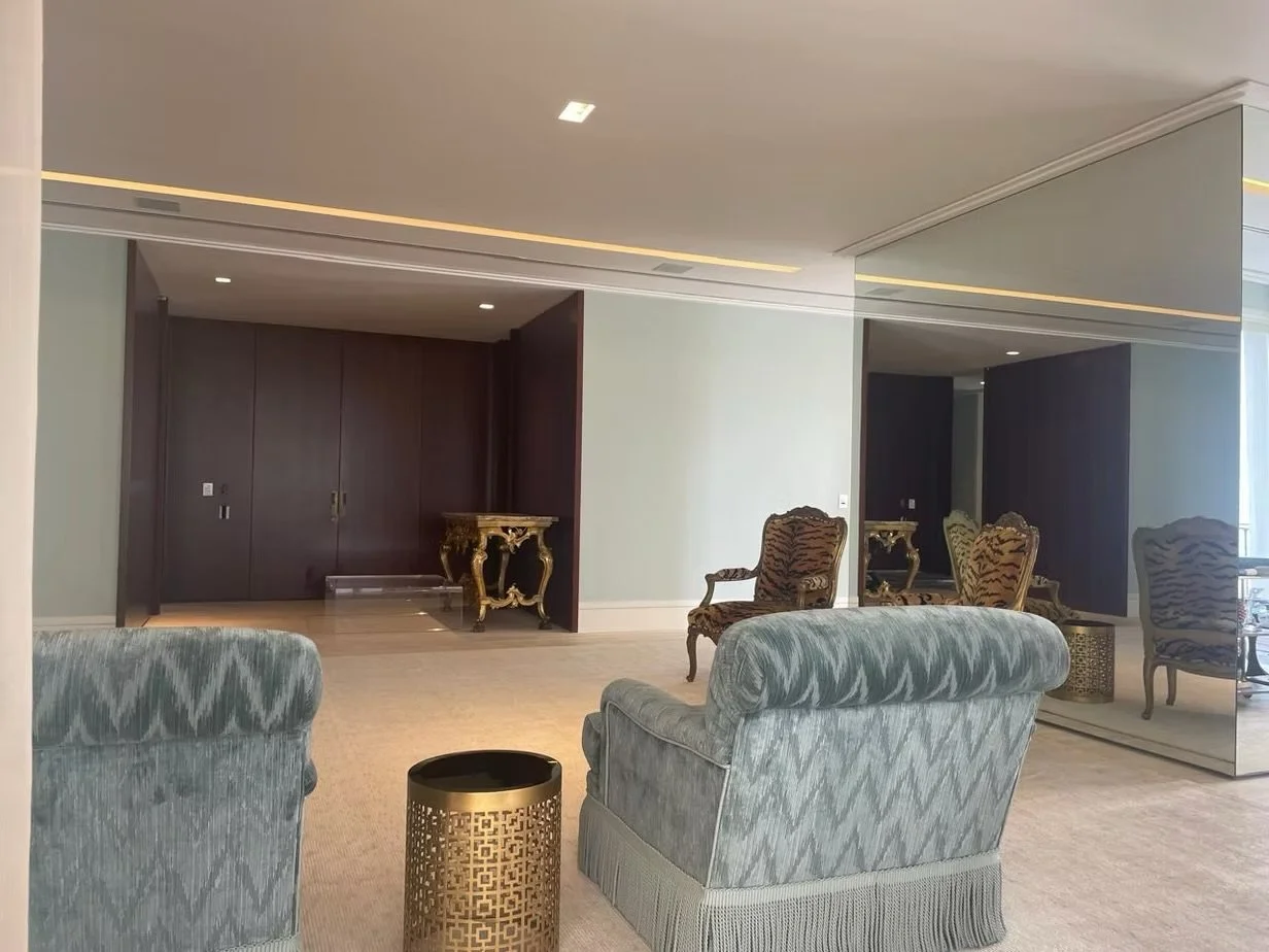 Sala de estar elegante com poltronas de estofado azul, cadeiras com estampa de tigre, tapete claro e espelho grande na parede, iluminação suave e móveis decorativos dourados.