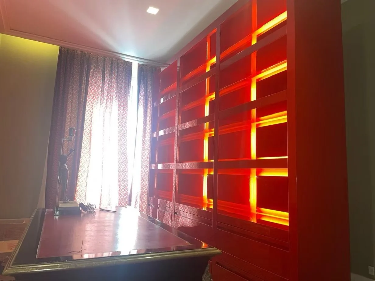 Sala com cortinas, escrivaninha de madeira, e uma estante de madeira com iluminação integrada