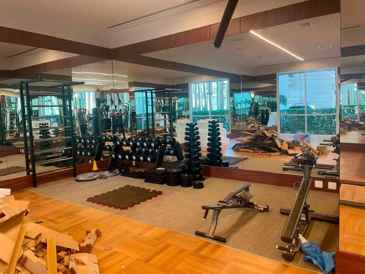 Sala de ginástica com espelhos na parede, pesos livres, esteiras e equipamentos de exercícios, todo organizado e preparado para treino.