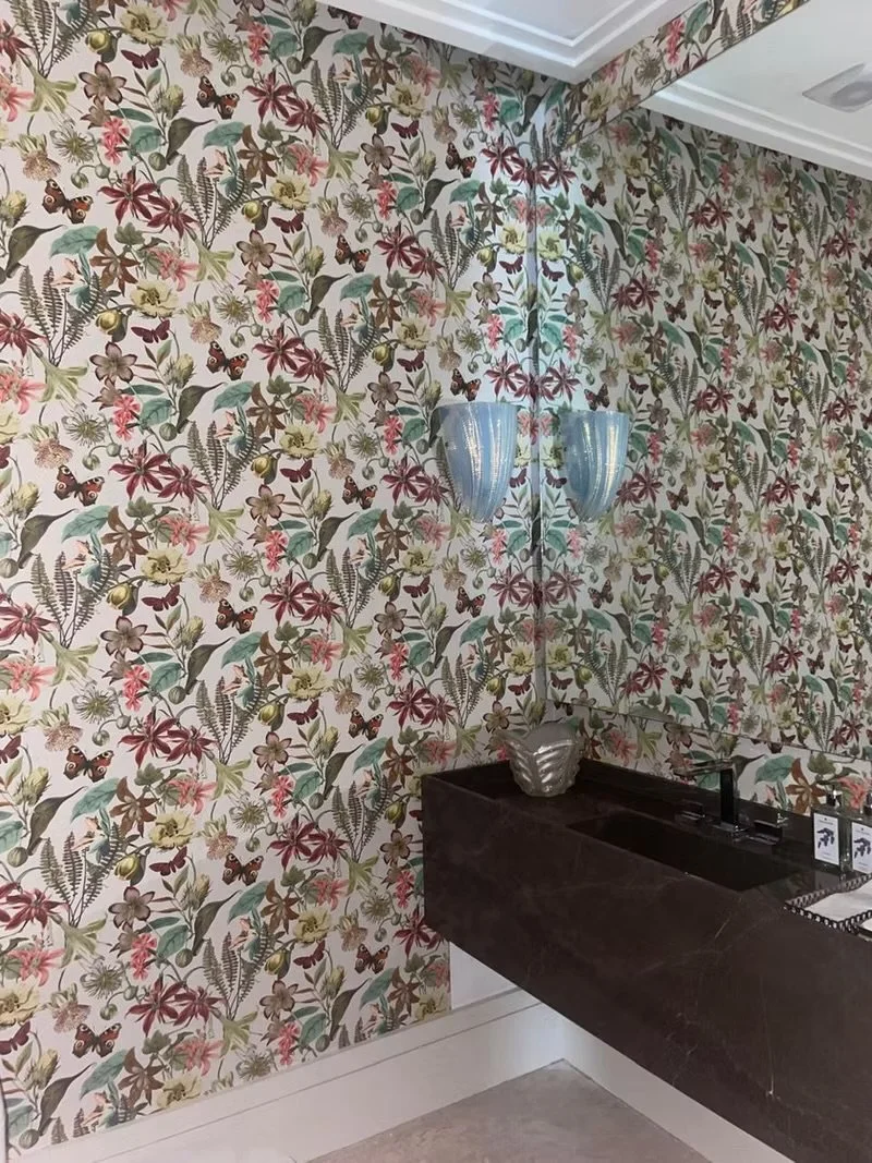 Parede com papel de parede floral com borboletas coloridas, espelho de canto e parede de mármore preto.