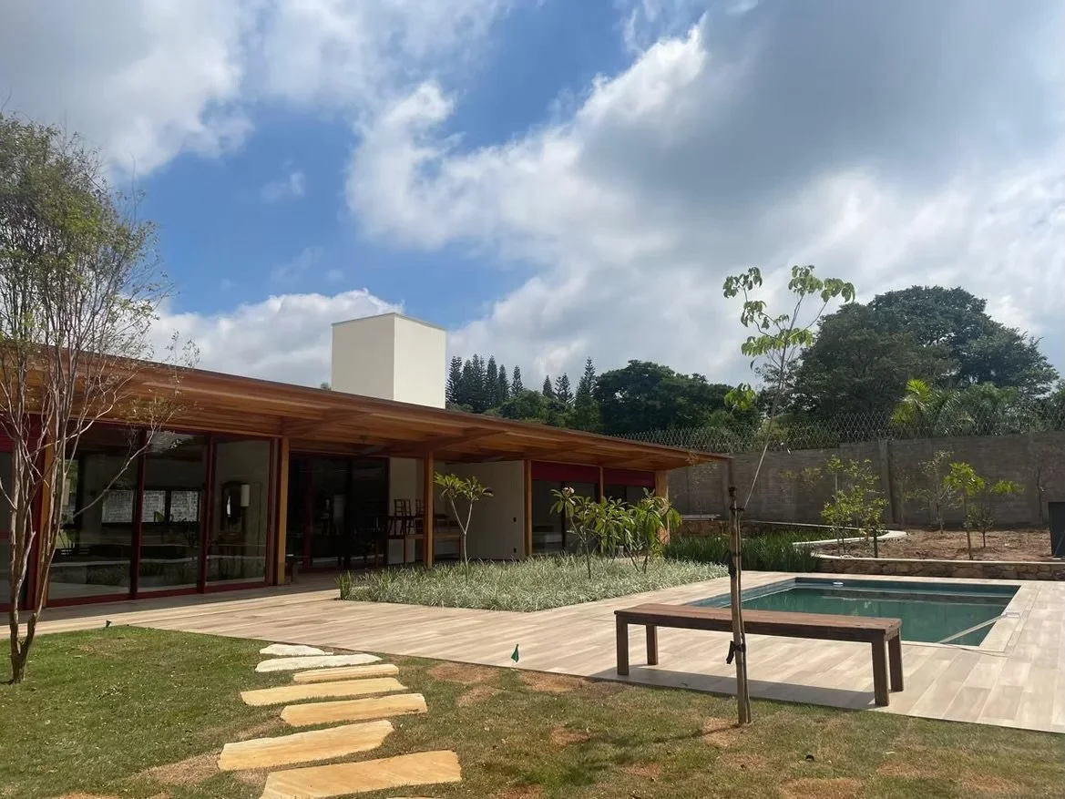 Casa moderna com piscina ao ar livre, jardim com árvores jovens e caminho de pedras, céu parcialmente nublado.