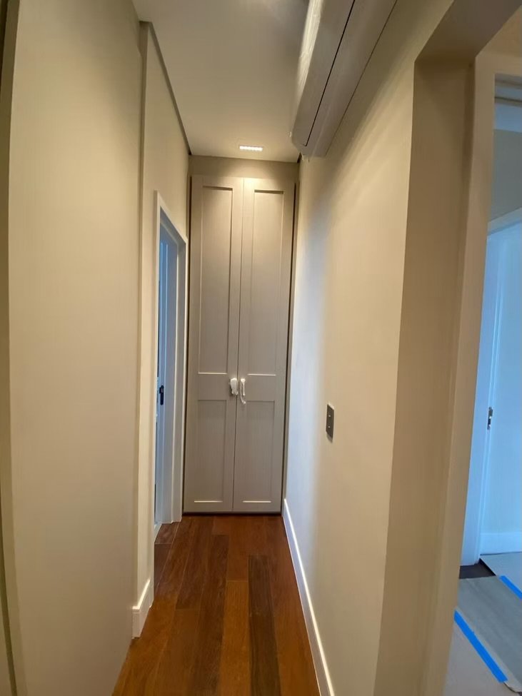 Corredor com piso de madeira clara, paredes bege e armário embutido na parede ao fundo, com porta dupla.