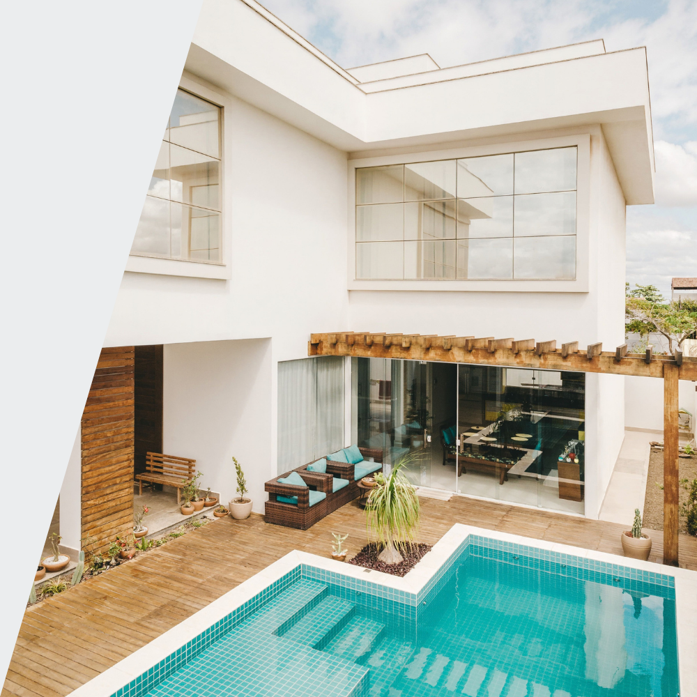 Modern white house with large glass windows, outdoor patio with seating, and a swimming pool with blue tiles.