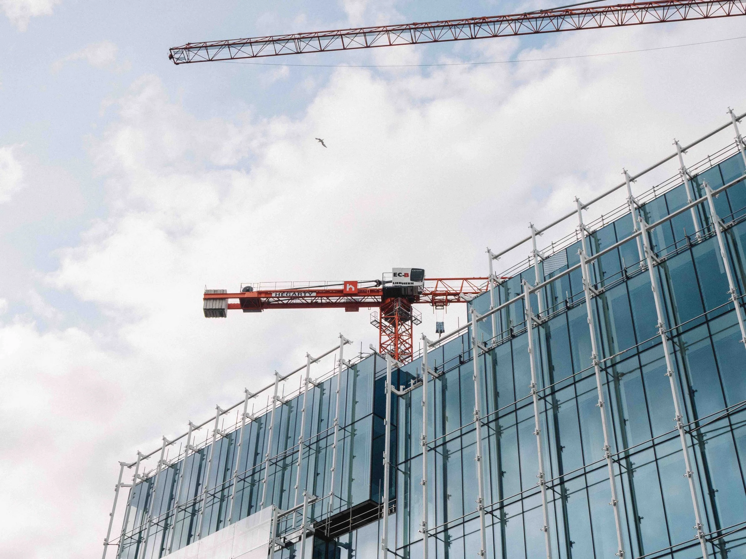 Construction crane over a modern glass building under construction on a cloudy day.