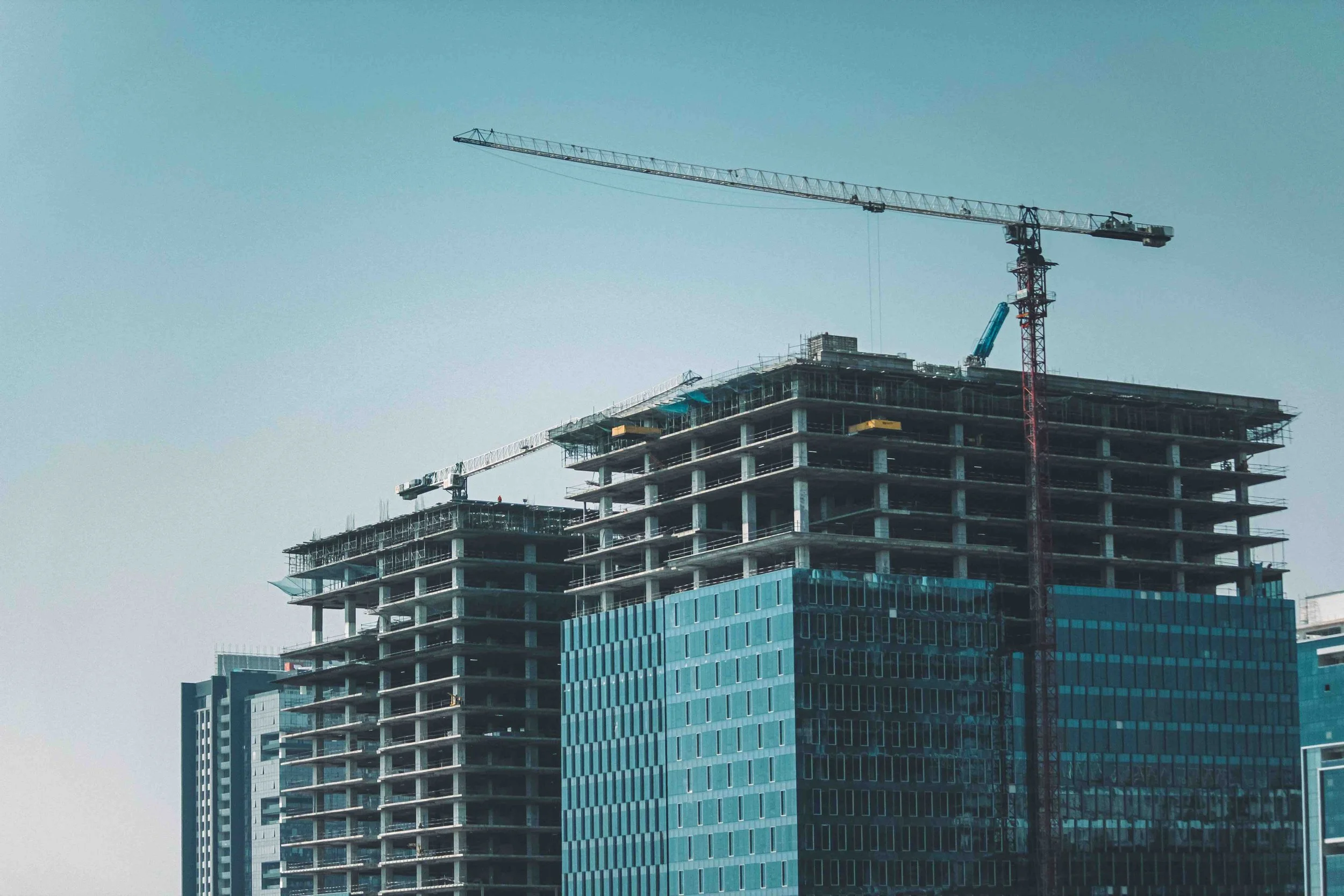 Modern high-rise building under construction with cranes on top.