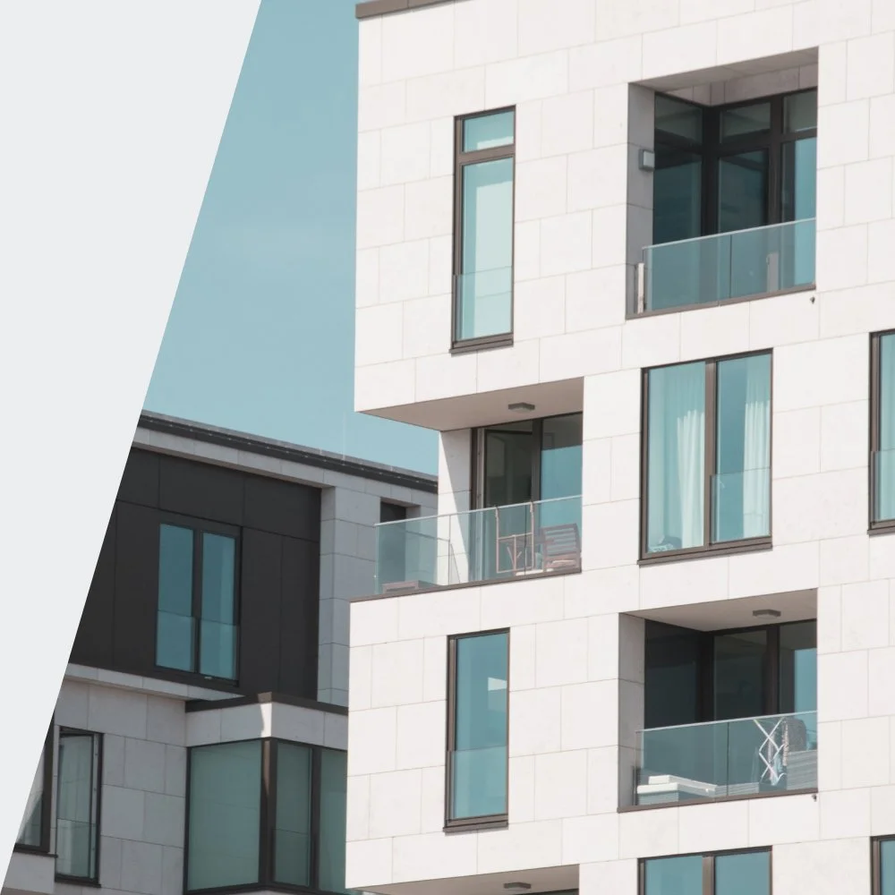 Modern apartment building with large glass windows and balconies, one balcony has cloth drying rack and furniture.