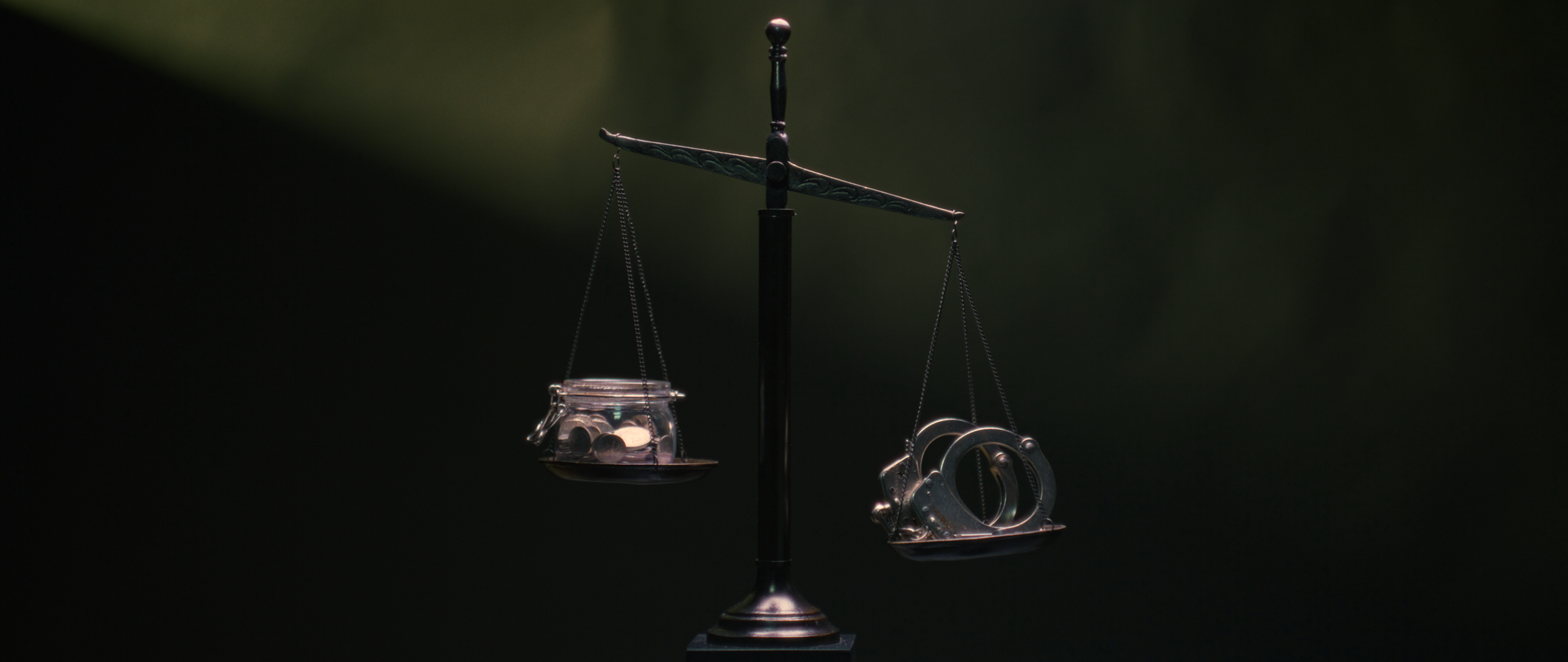 A balance scale with a jar of coins on one side and handcuffs on the other.