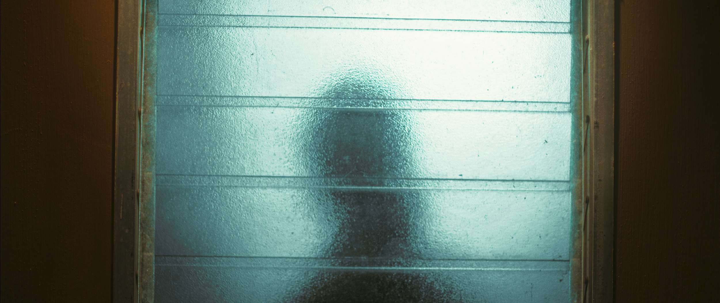A person standing behind a textured glass window, with their silhouette slightly visible through the frosted glass.