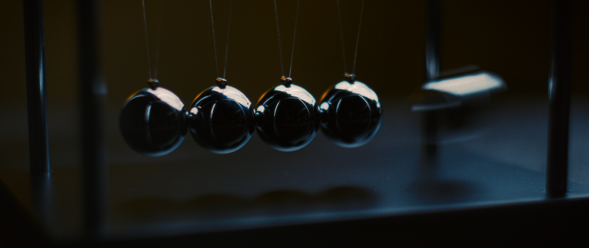 Close-up of a Newton's cradle with shiny black spheres suspended from strings, set against a dark background.