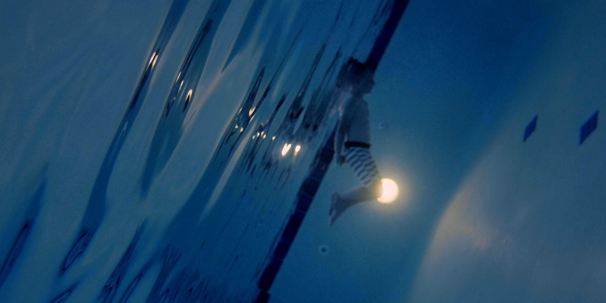 A person in a swimming pool at night, illuminated by moonlight.