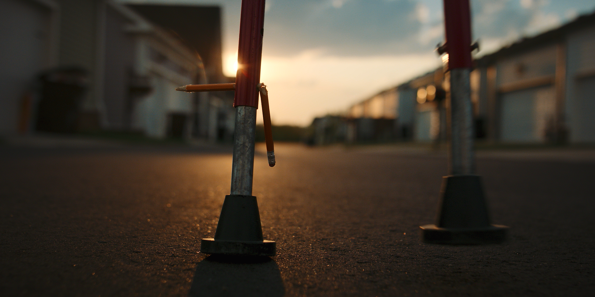 Image of a construction cone and a pencil stuck in the ground on an empty street during sunset.