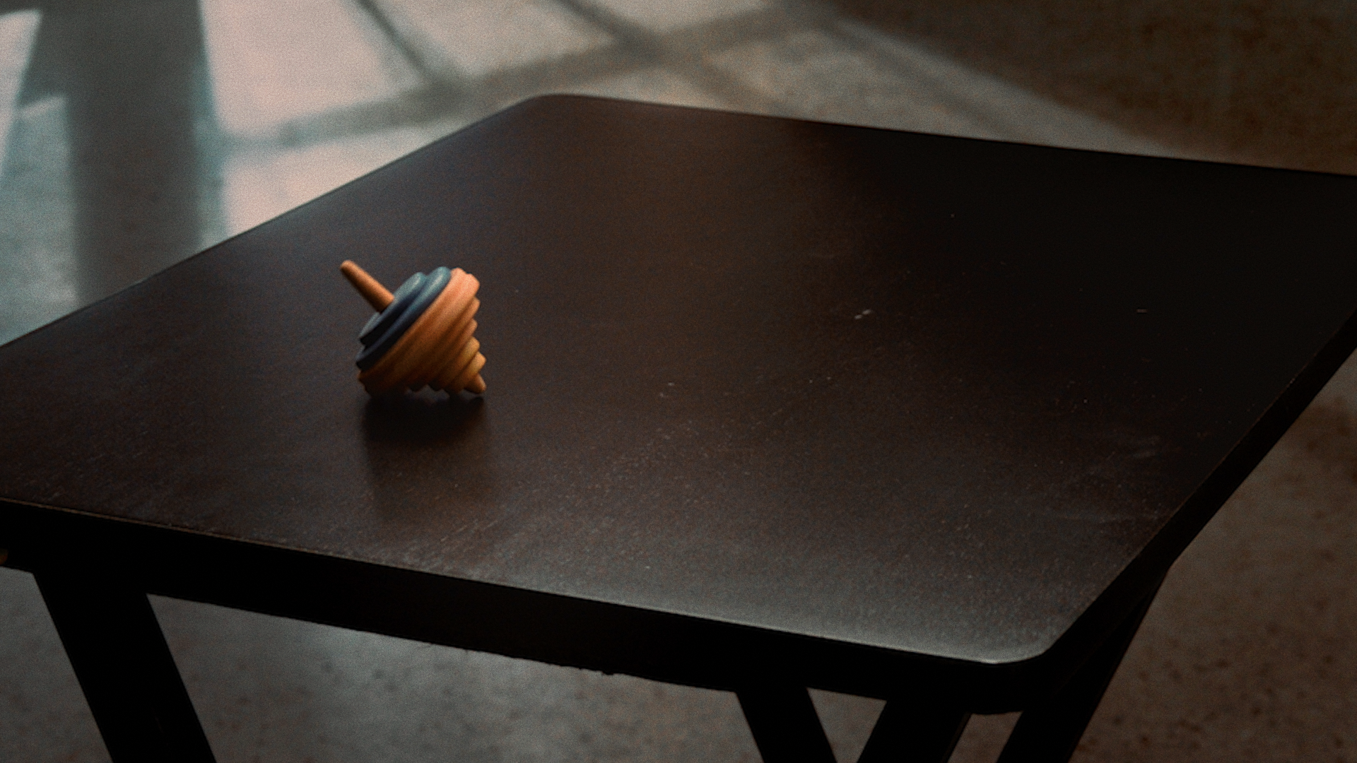 A swirling wooden spinning top resting on a dark, textured table in a dimly lit room.