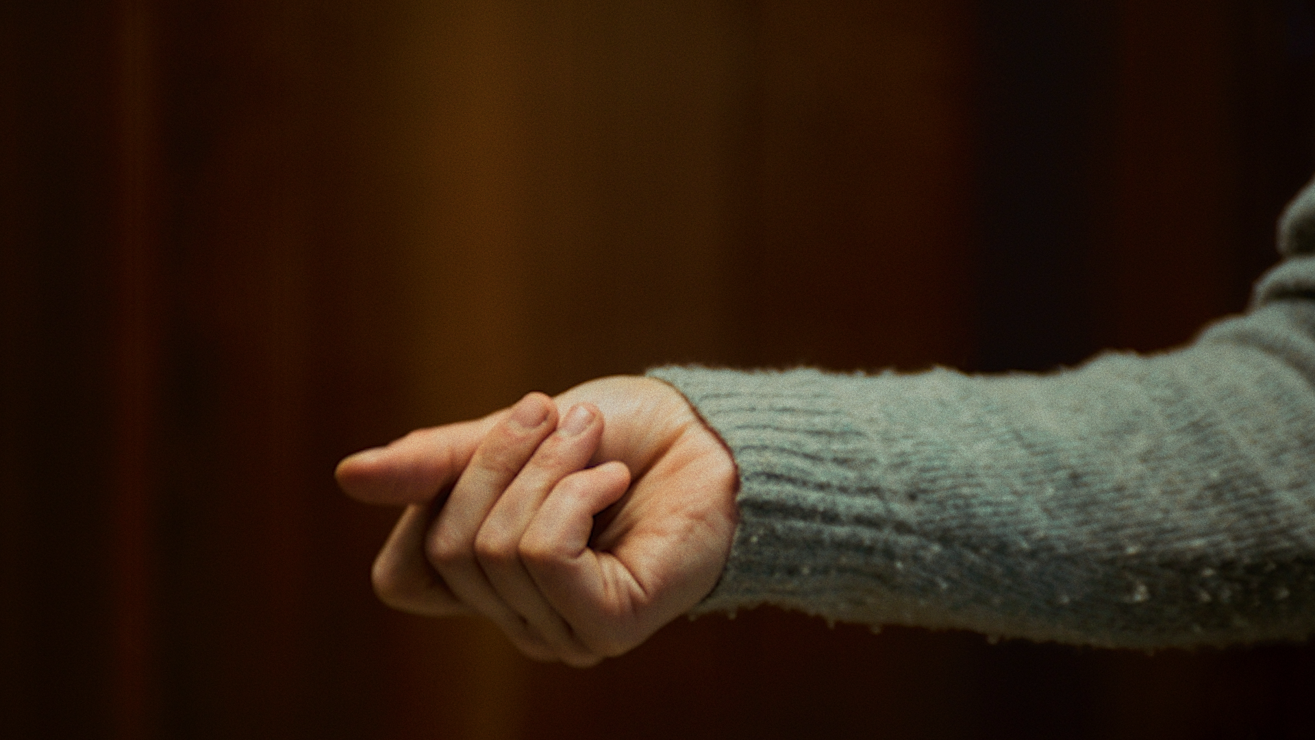 Close-up of two people holding hands in an embrace, with one person's hand gently grasping the other's hand, against a dark background.