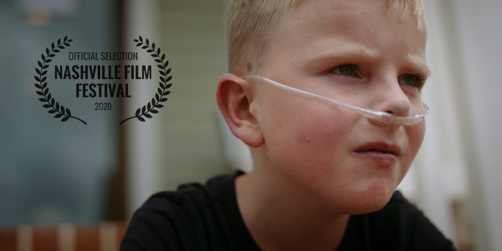Young boy with blond hair and green eyes, wearing a nasal cannula, looking to the side, with a Nashville Film Festival 2020 official selection logo overlayed on the image.