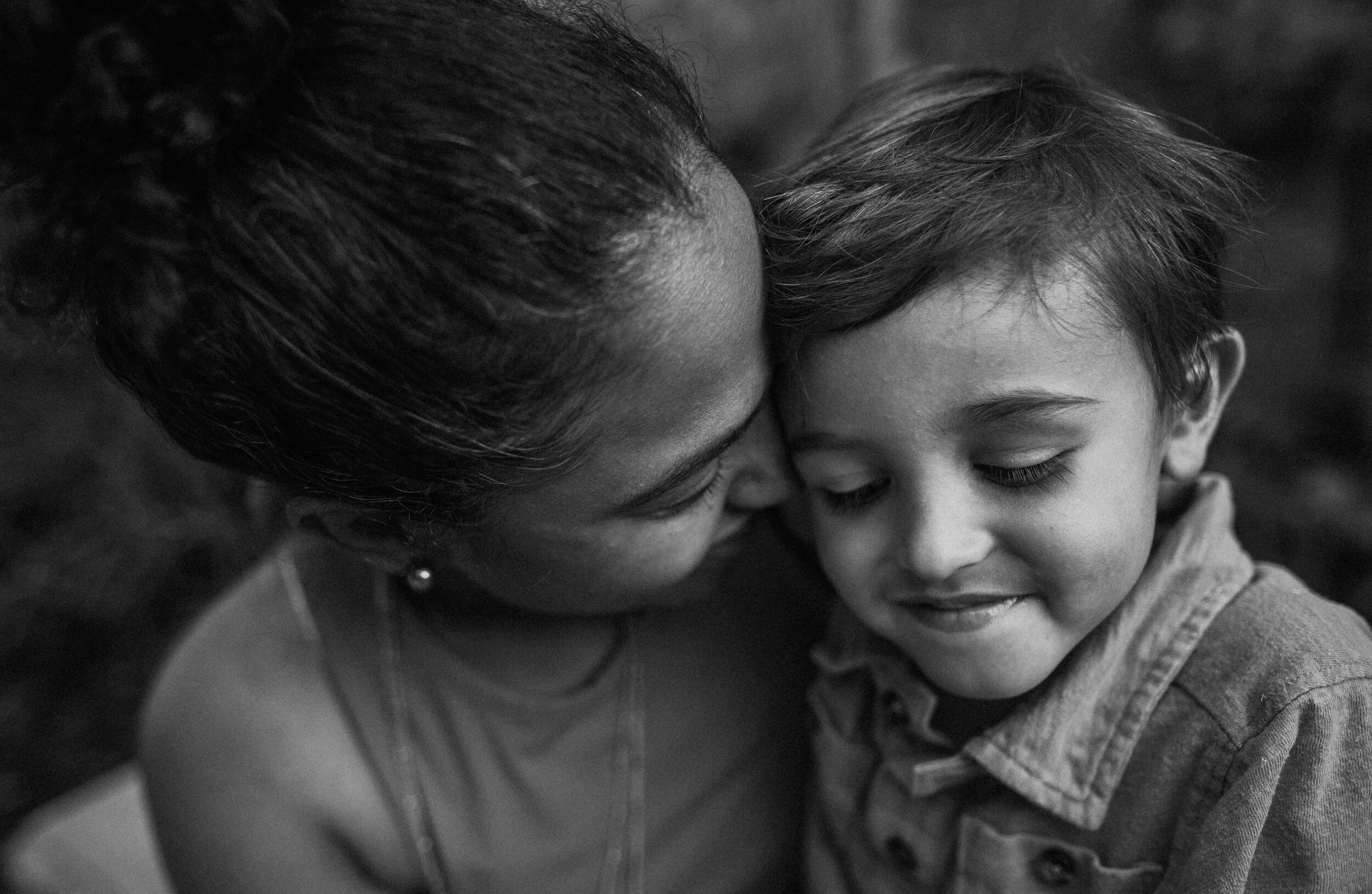 A black and white close-up photo of a woman and a young child sharing a gentle, tender moment with their foreheads touching and eyes closed, showing affection and emotional connection.