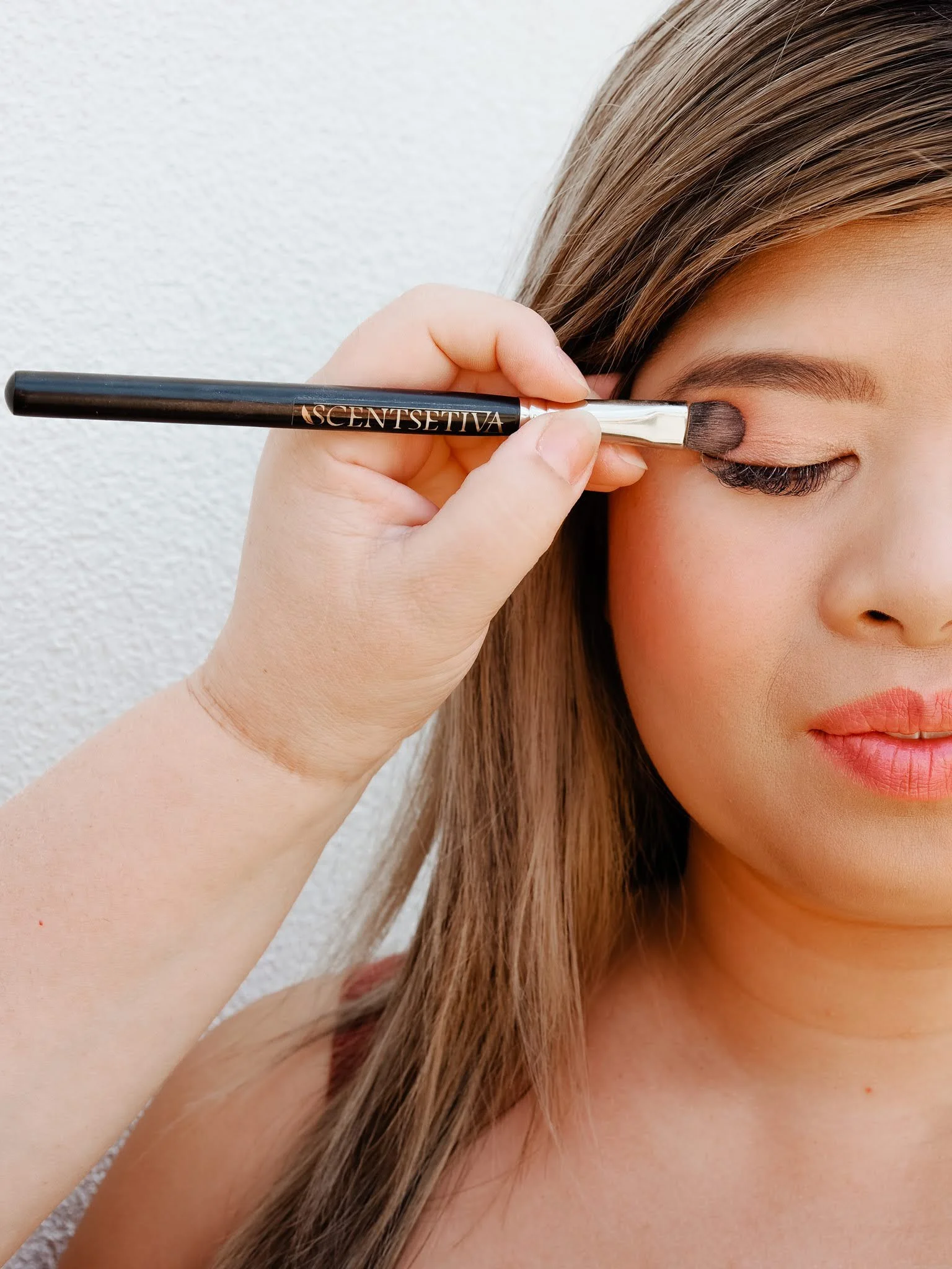 Close-up of a woman applying makeup with a brush to her eyelid.