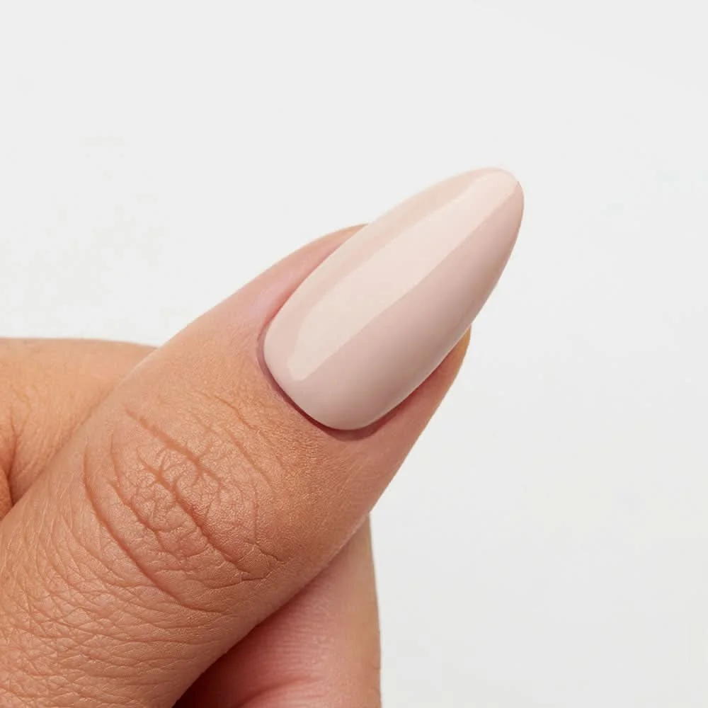 A close-up of a thumb with neatly manicured, glossy, light beige or nude-colored nail polish.