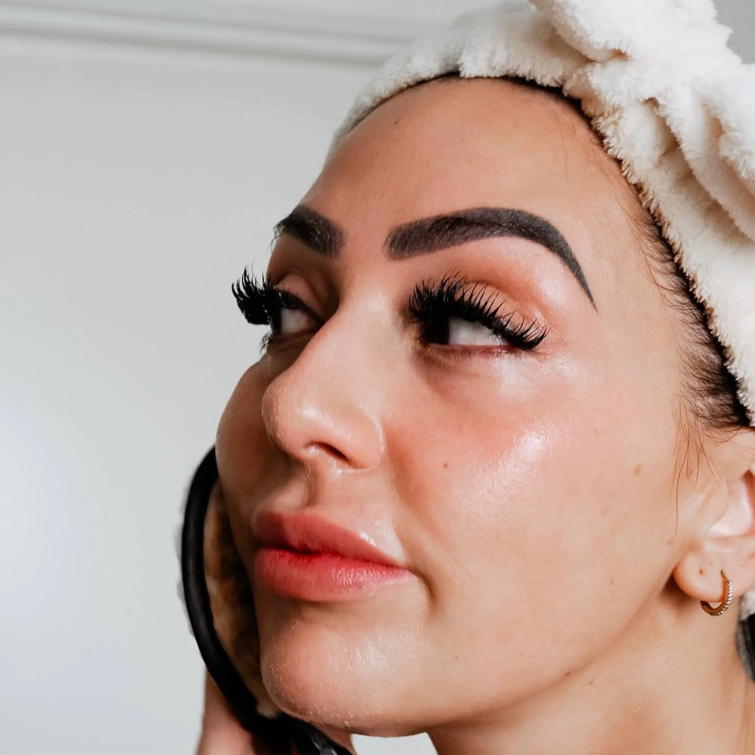 Close-up of a woman with dark eyebrows, long eyelashes, and makeup, wrapped in a white towel.