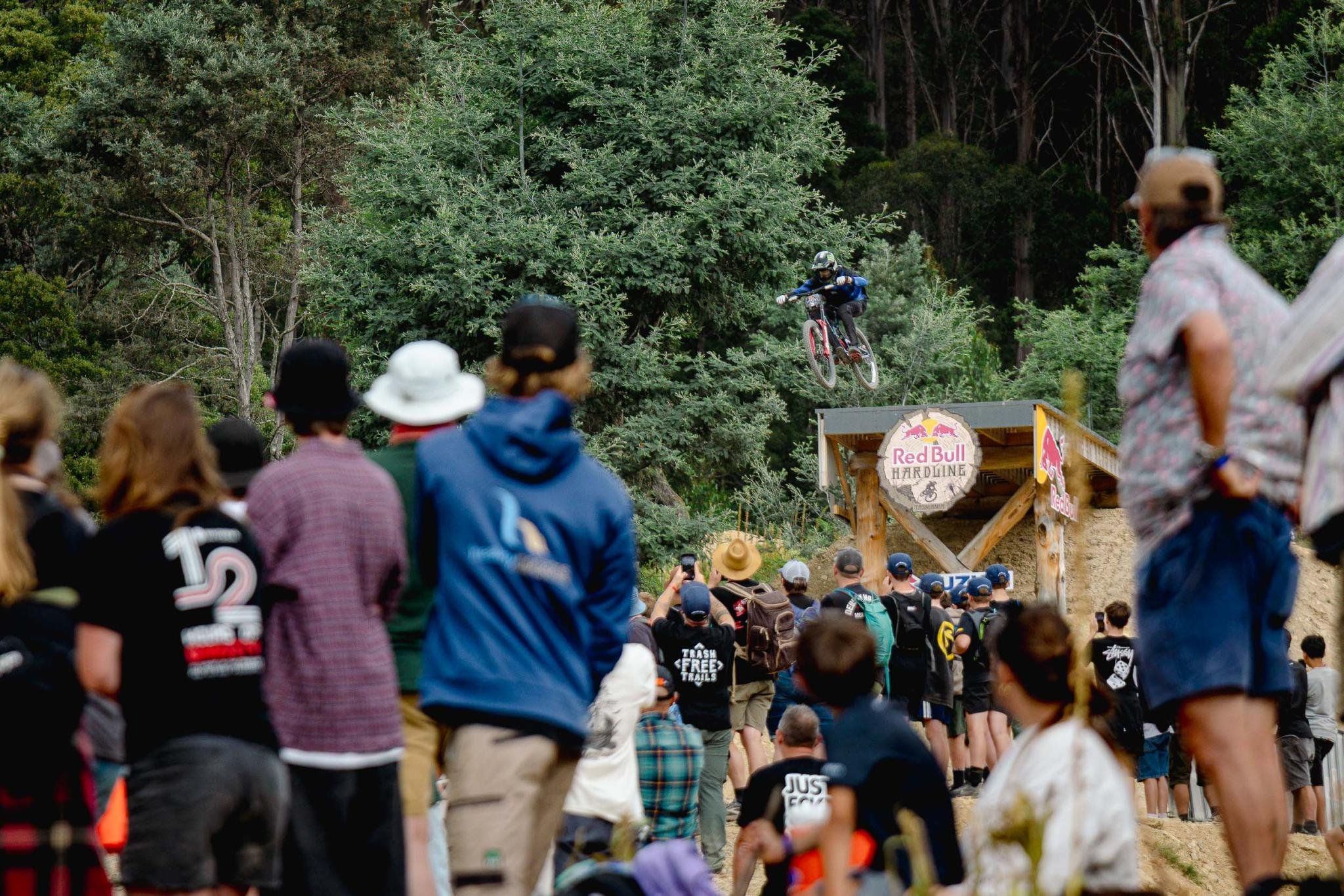 Bambino in corsa durante una gara di mountain bike in un bosco con pubblico e loghi di Red Bull sulla pista.