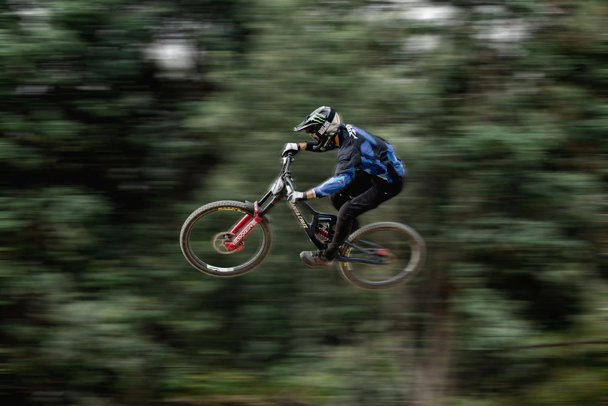 Un motociclista che fa downhill in un bosco con alberi verdi sfocati a causa della velocità.