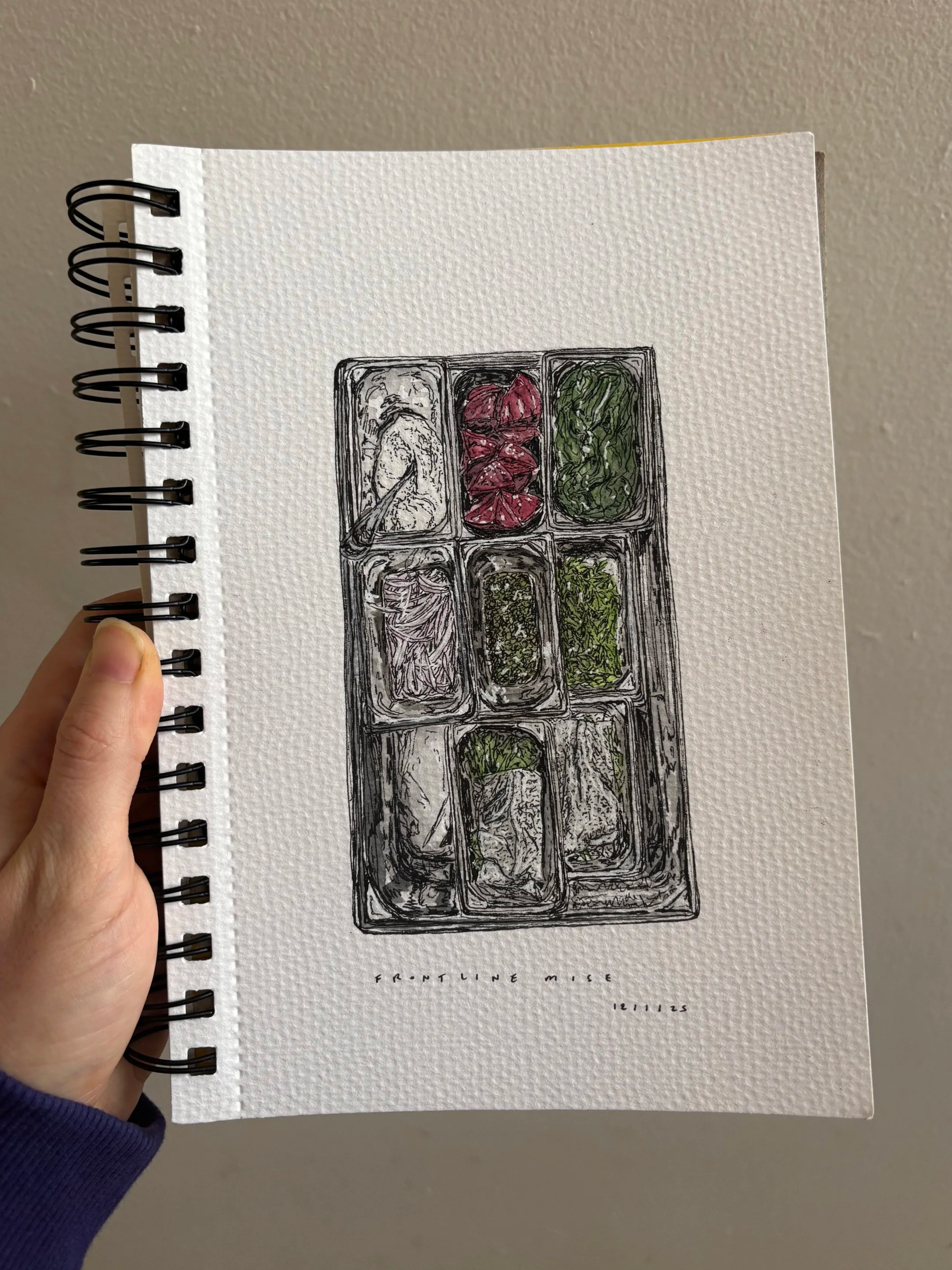 A person holding a spiral-bound notebook with a hand-drawn illustration of a food container filled with various ingredients labeled "Frontline Nise" and a date of "12/11/25."