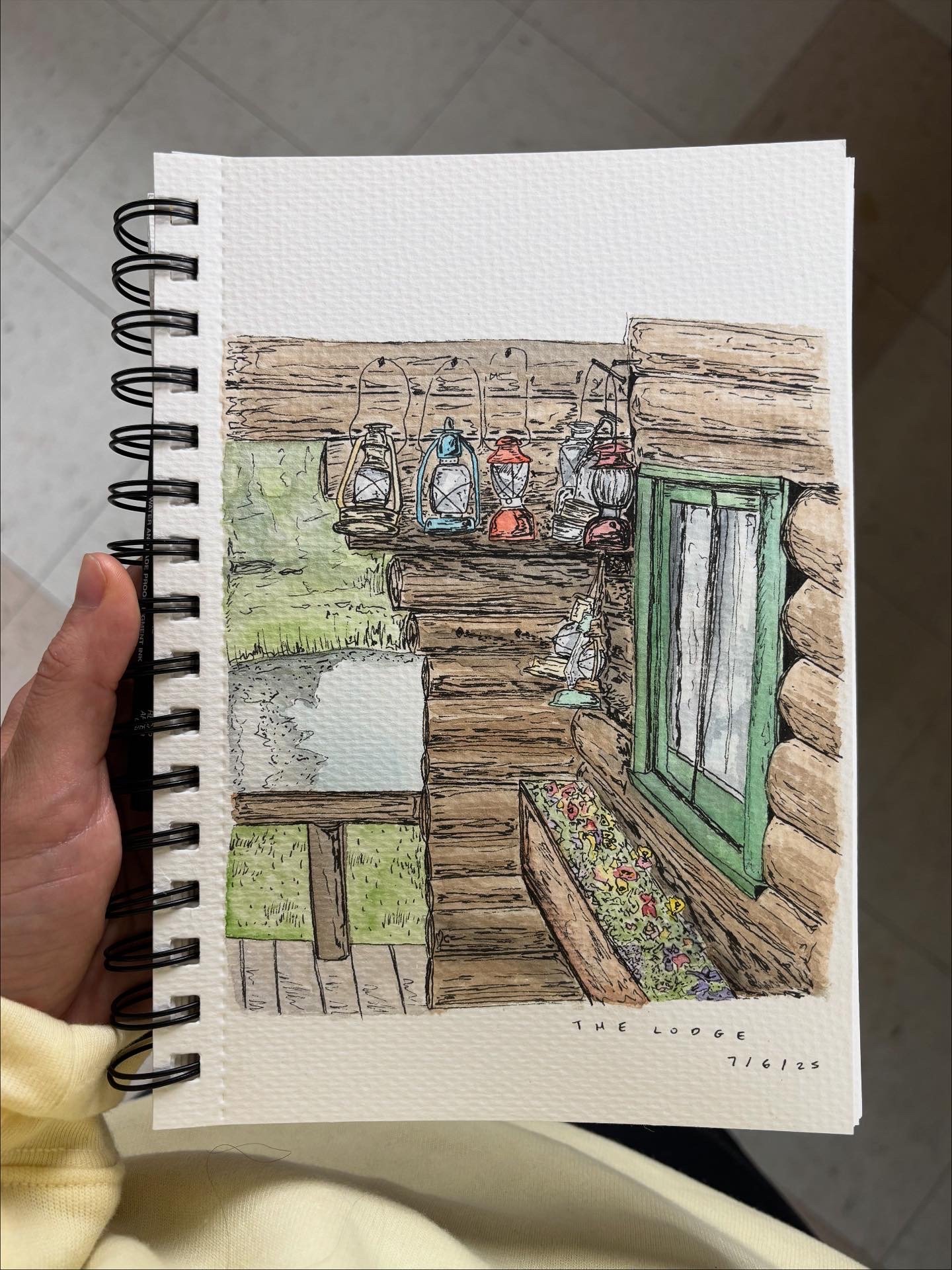 Colorful illustration of a rustic log cabin exterior, showing a wooden table with lamps, a green cabinet, a window with flowers, and a view outside with green foliage.