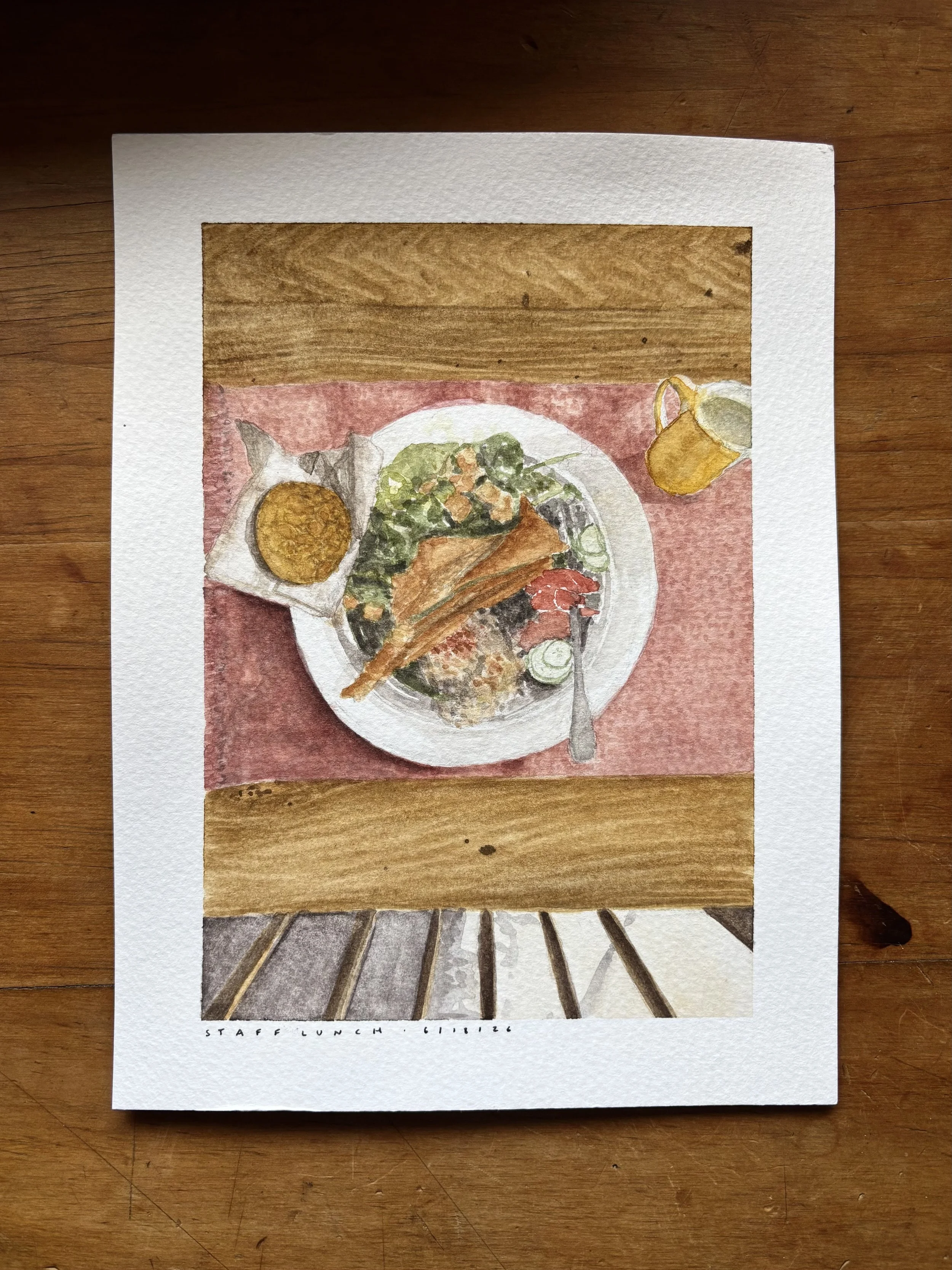 A watercolor painting of a staff lunch sitting on a wooden table. The lunch includes a plate of salad with greens and vegetables, a piece of bread or toast, a cookie or biscuit, and a cup of coffee or tea.