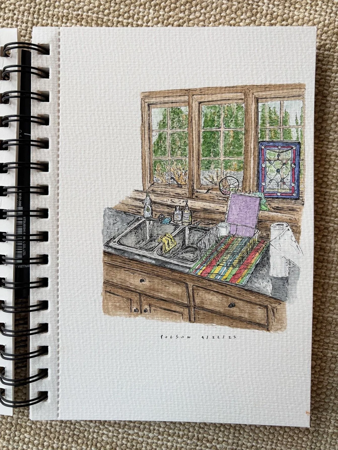 A watercolor painting of a kitchen with a double sink, wooden cabinets, and a large window showing green trees outside. There are soap bottles by the sink, a dishcloth, a purple chair with a colorful striped blanket, and some decorative items includi