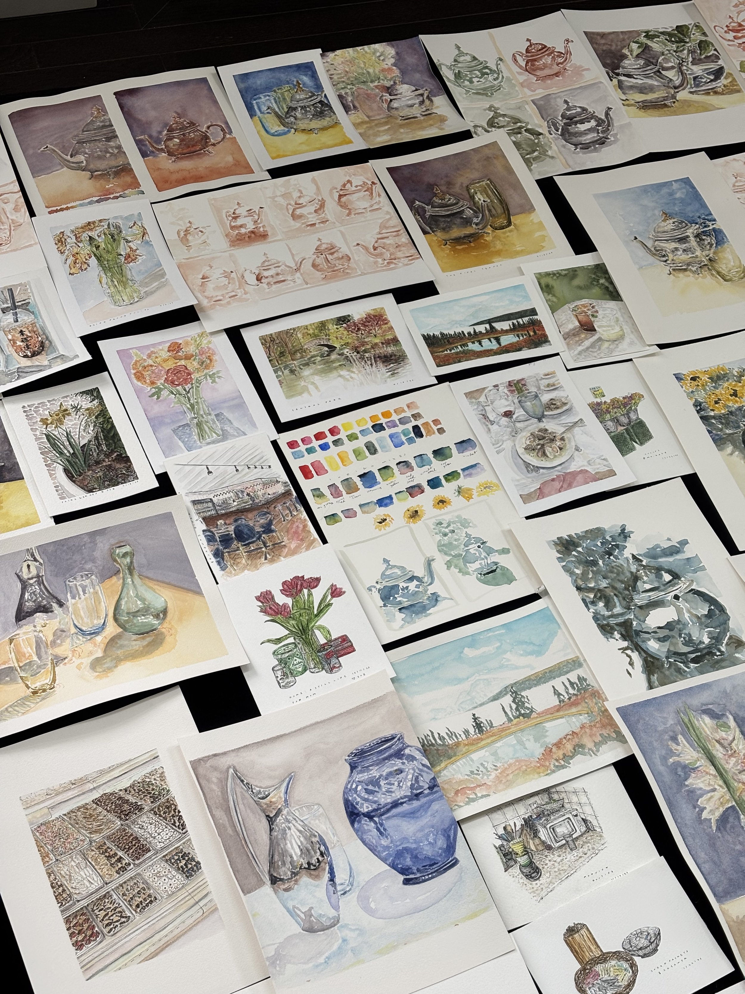 Collection of watercolor paintings of various objects, landscapes, still life scenes, and floral arrangements arranged on a flat surface.