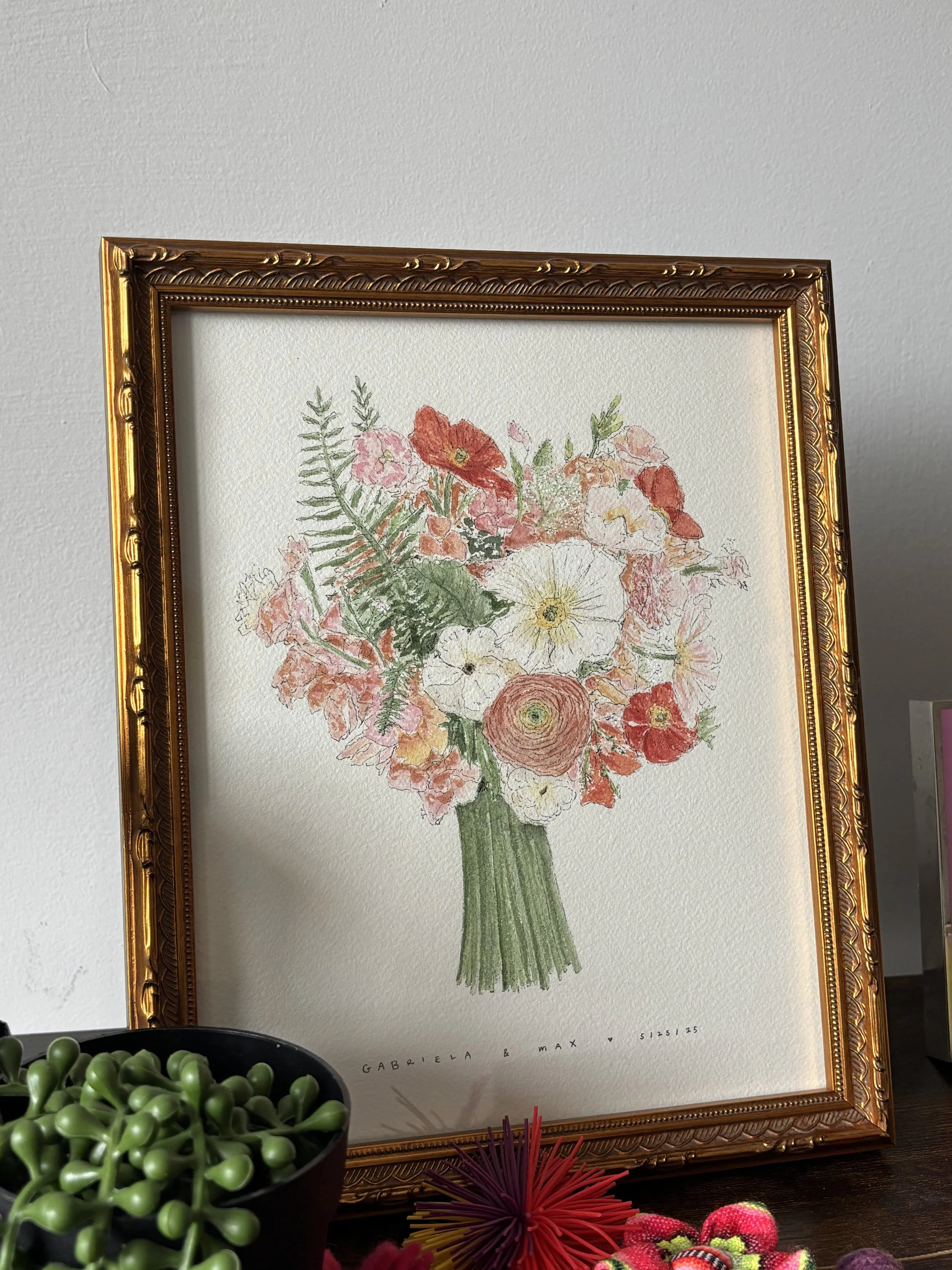 A framed watercolor painting of a bouquet of pink, orange, and white flowers with green leaves, mounted on a white wall. 