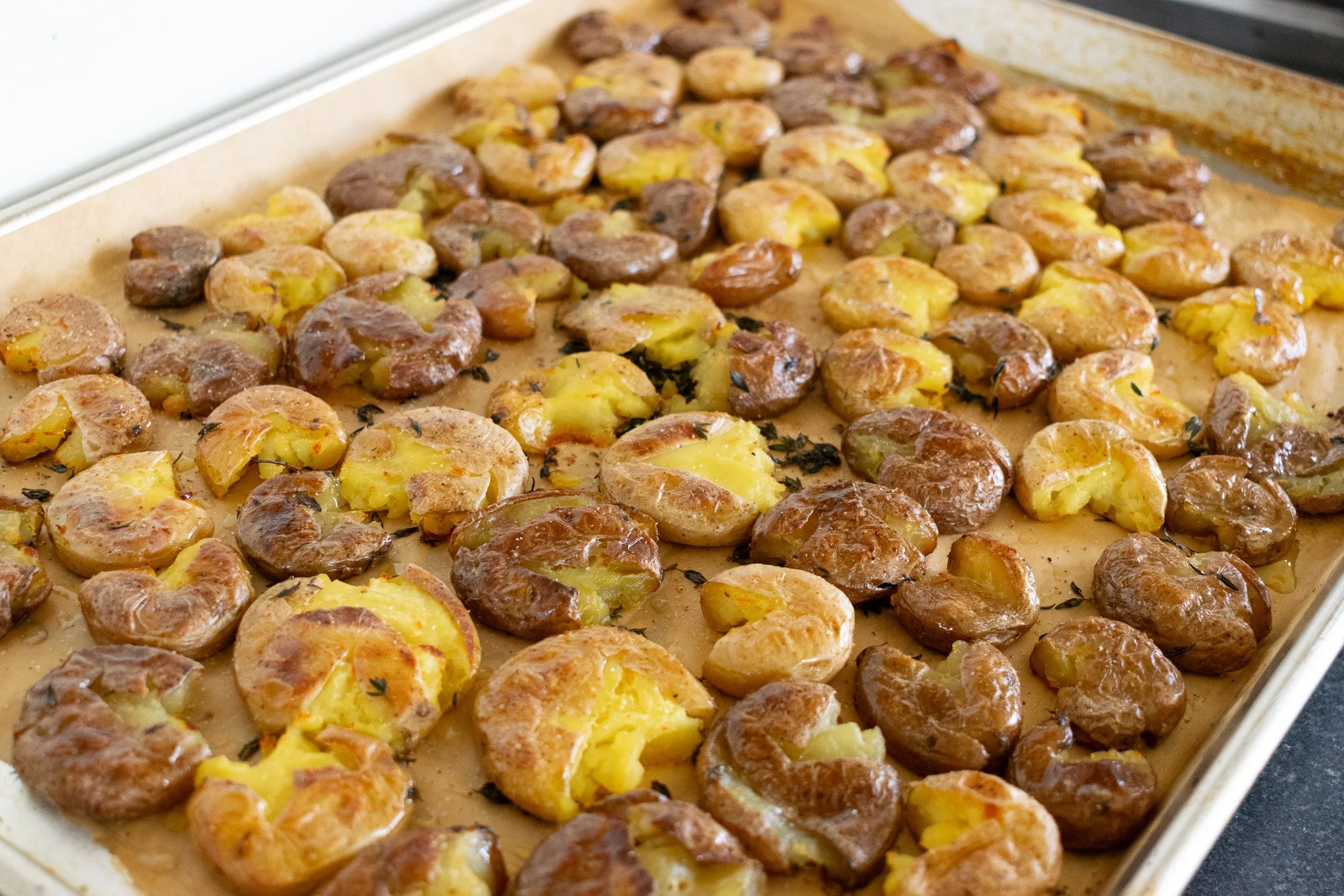 Baked potatoes with cheese and herbs on a baking sheet.