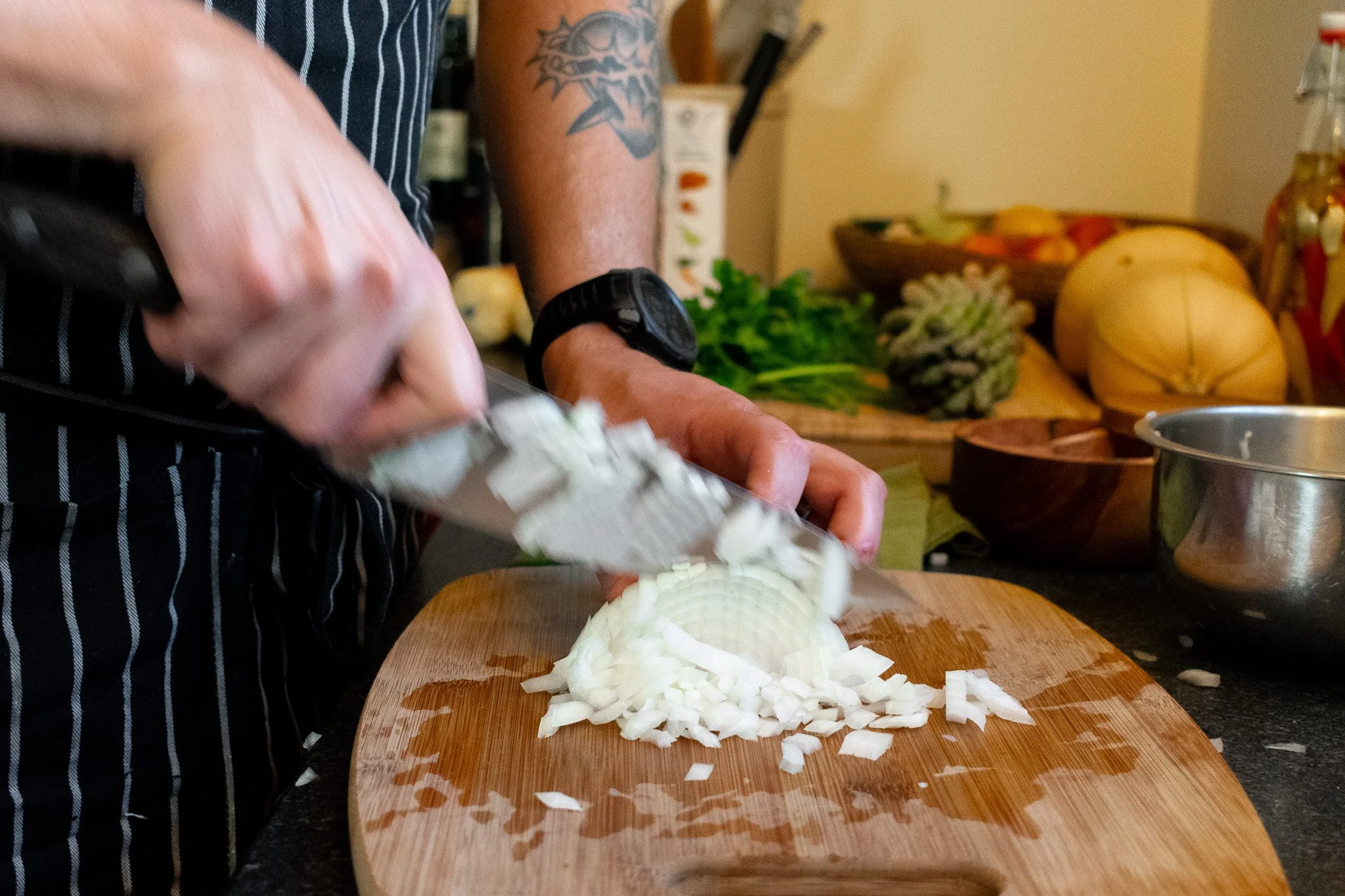 Person chopping a white onion on a wooden cutting board in a kitchen.
