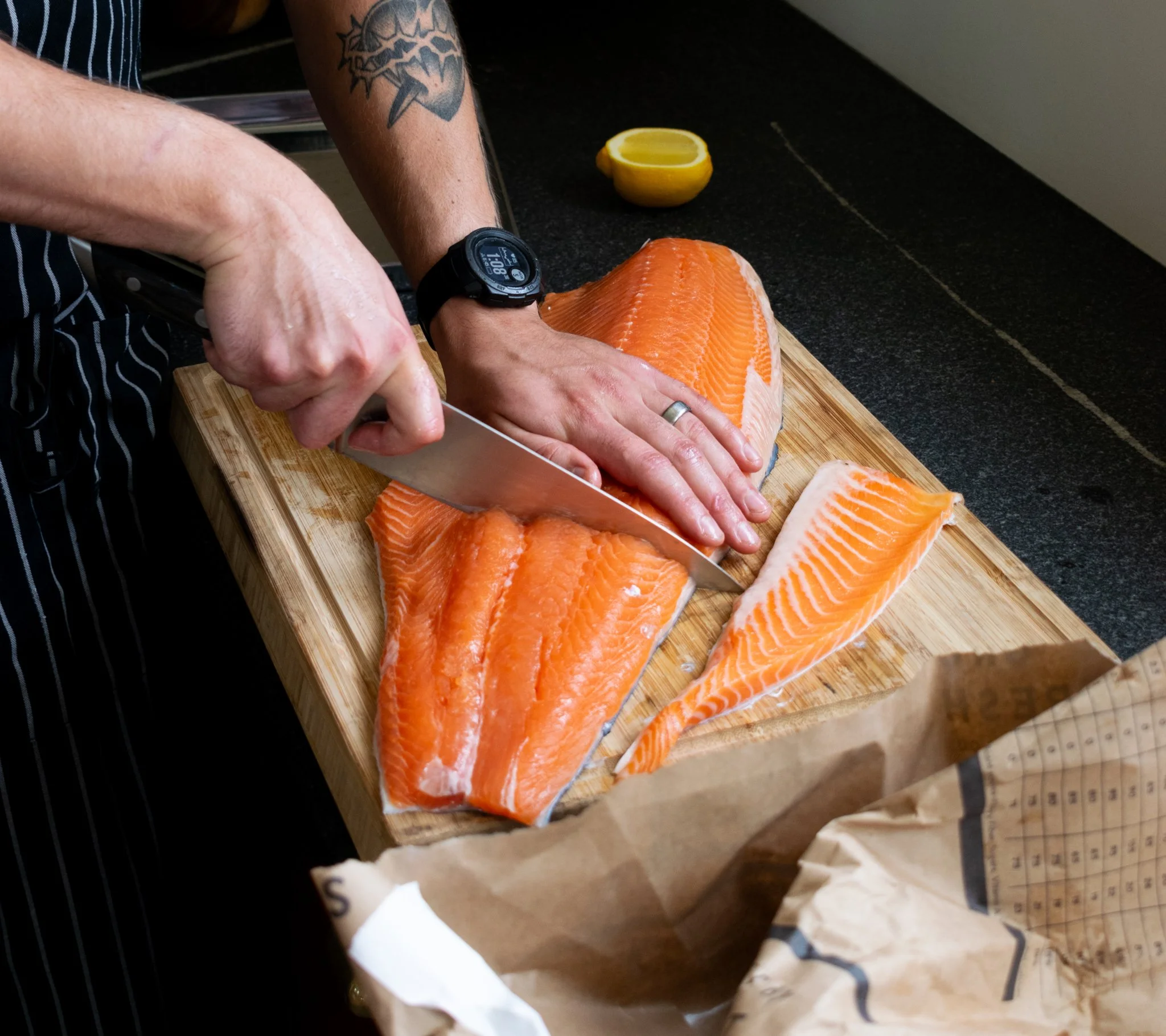 Person slicing fresh salmon fillet on a wooden cutting board, with lemon halves in the background.