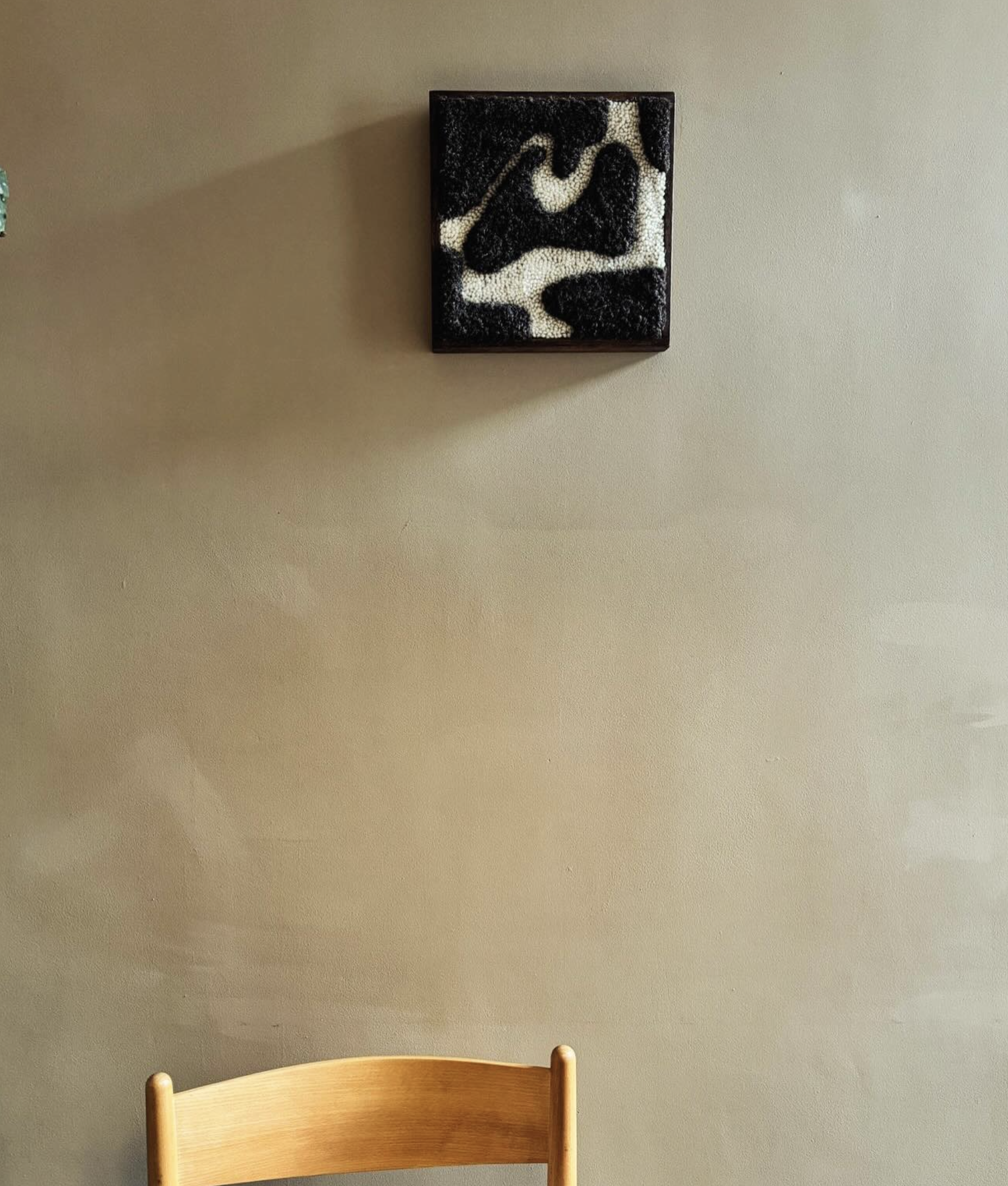 A wooden chair with a curved backrest in front of a plain beige wall. Above the chair, there is a framed abstract black and white textured art piece.