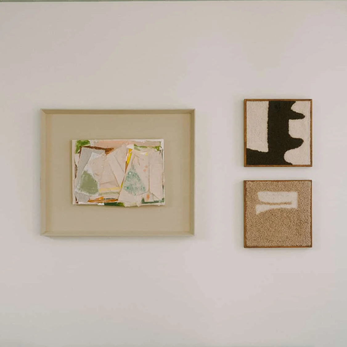 Three abstract art pieces hanging on a white wall, with the larger piece in a frame on the left and two smaller pieces stacked vertically on the right.
