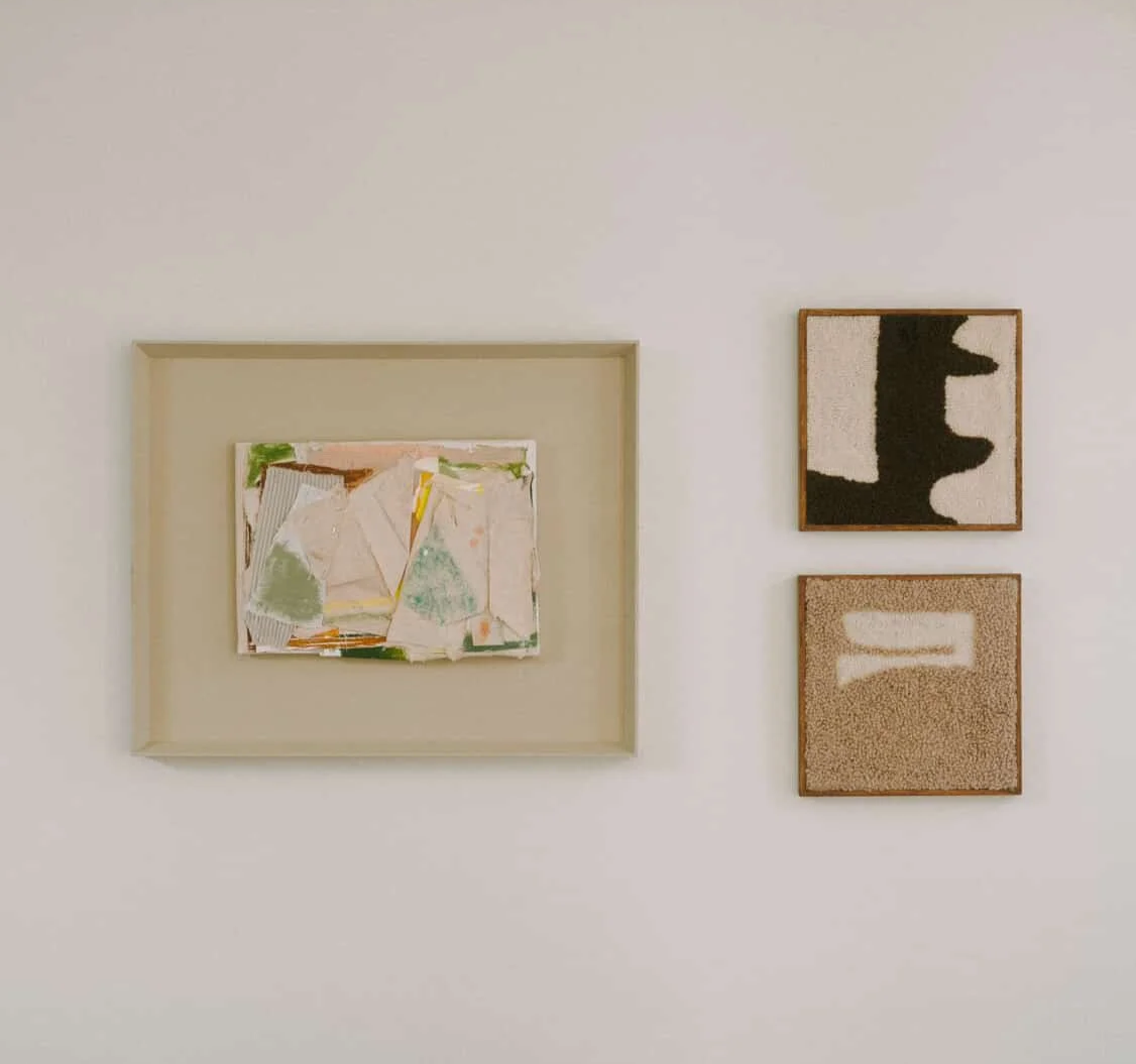 Three abstract art pieces on a white wall, with a large mixed-media piece in a light-colored frame on the left and two smaller pieces, one in black and white and the other in beige, on the right.