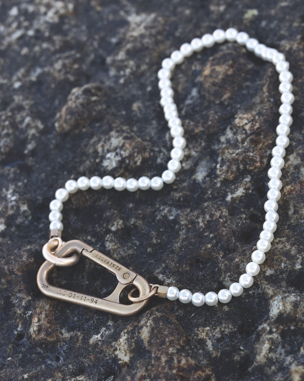 A pearl necklace with a metal clasp lying on a textured dark stone surface.