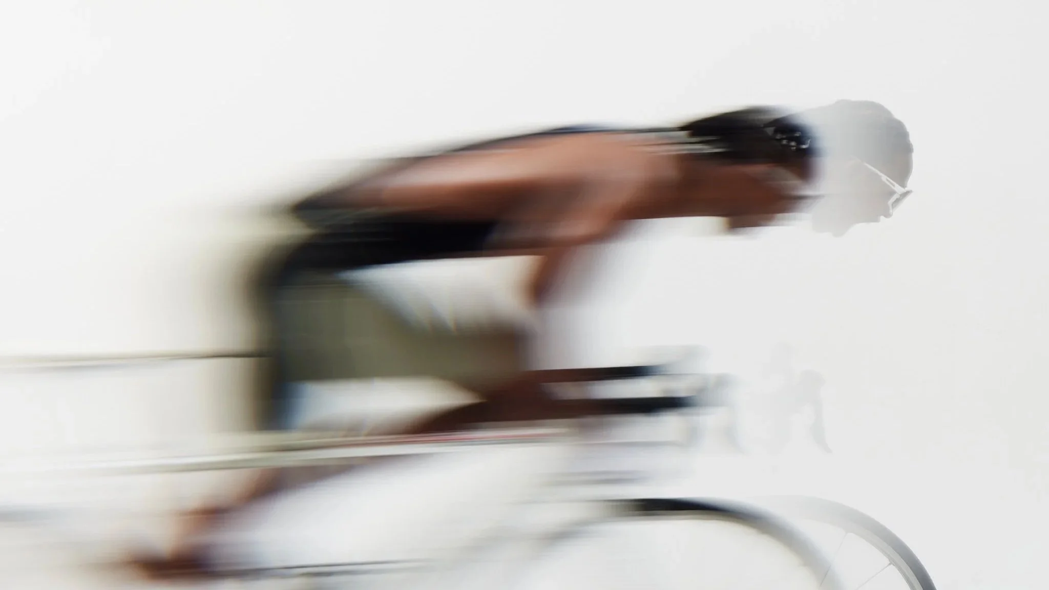 A blurred person wearing sunglasses and a tank top, standing in front of a white wall.