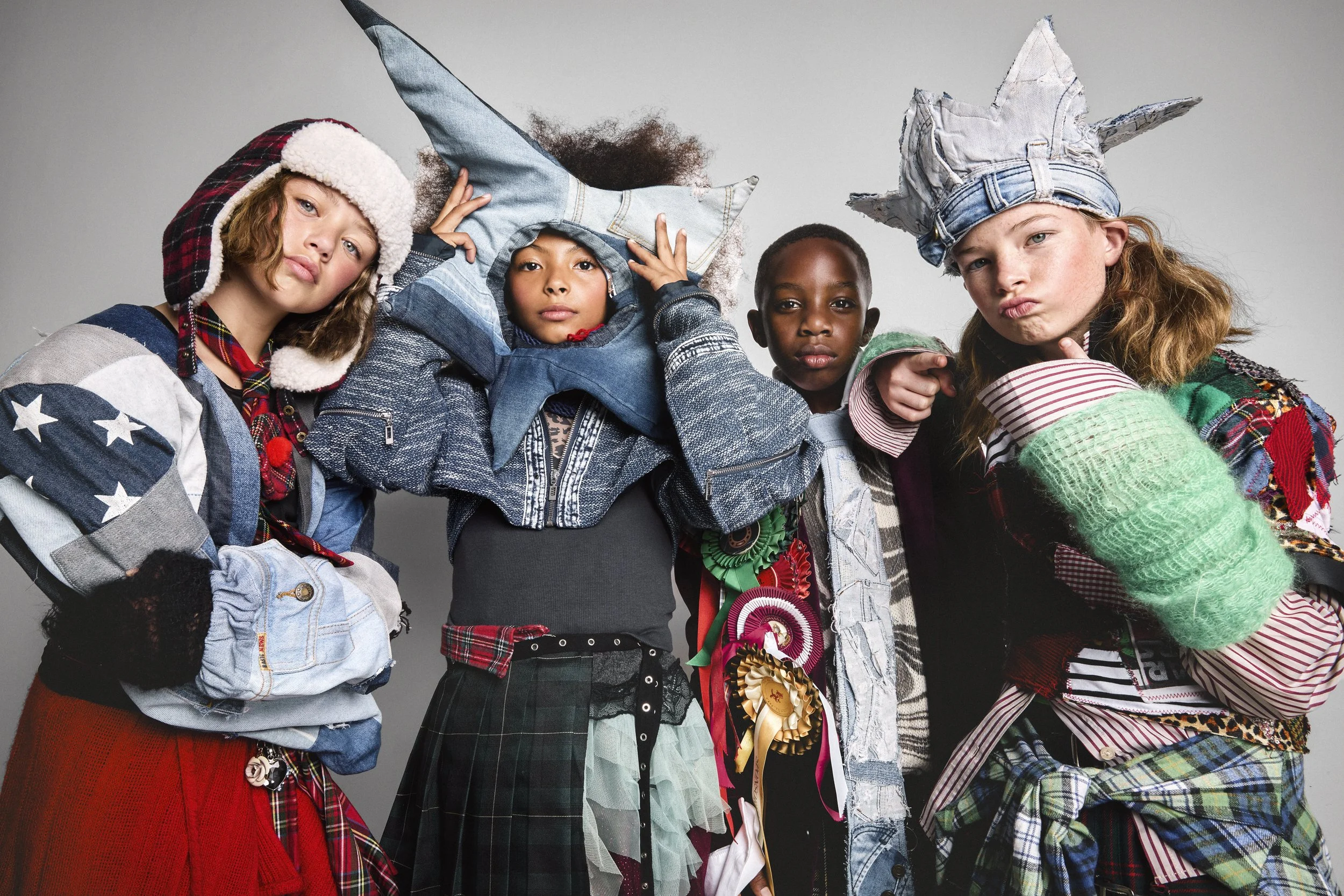 Four children dressed in colorful, eclectic outfits, with some wearing hats made from denim and other fabrics, posing together for a photo.