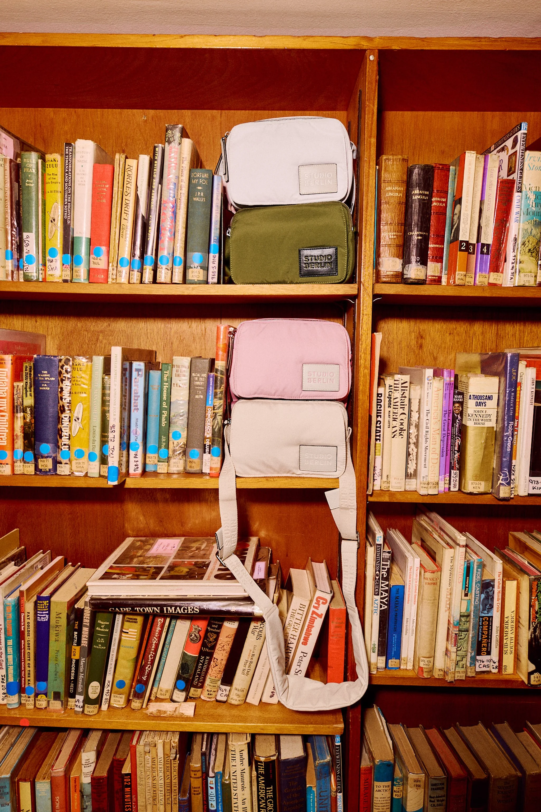 A wooden bookshelf filled with various books, with four small colored bags placed on the middle shelves.