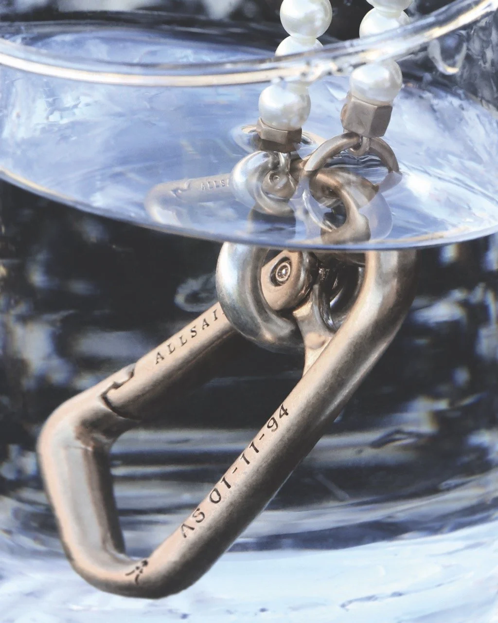 Close-up of scuba diving or climbing metal carabiners attached to a clear plastic surface, with water visible inside.