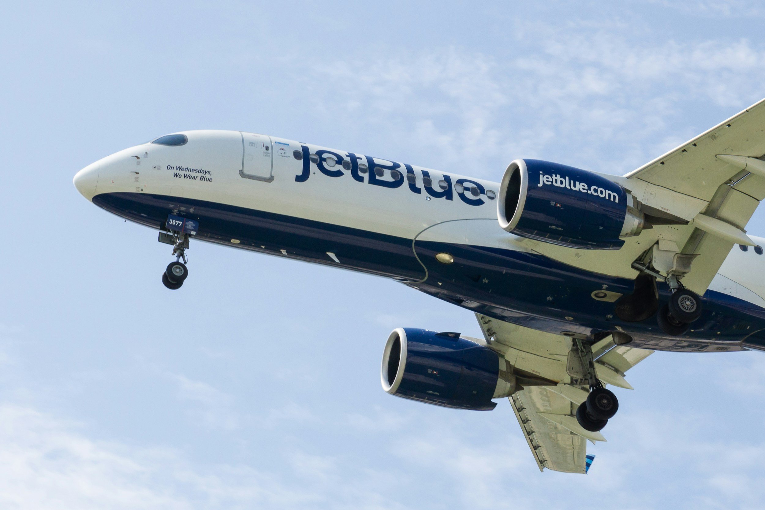Front view of a JetBlue airplane in flight, displaying the JetBlue logo on the fuselage and engines against a cloudy sky.