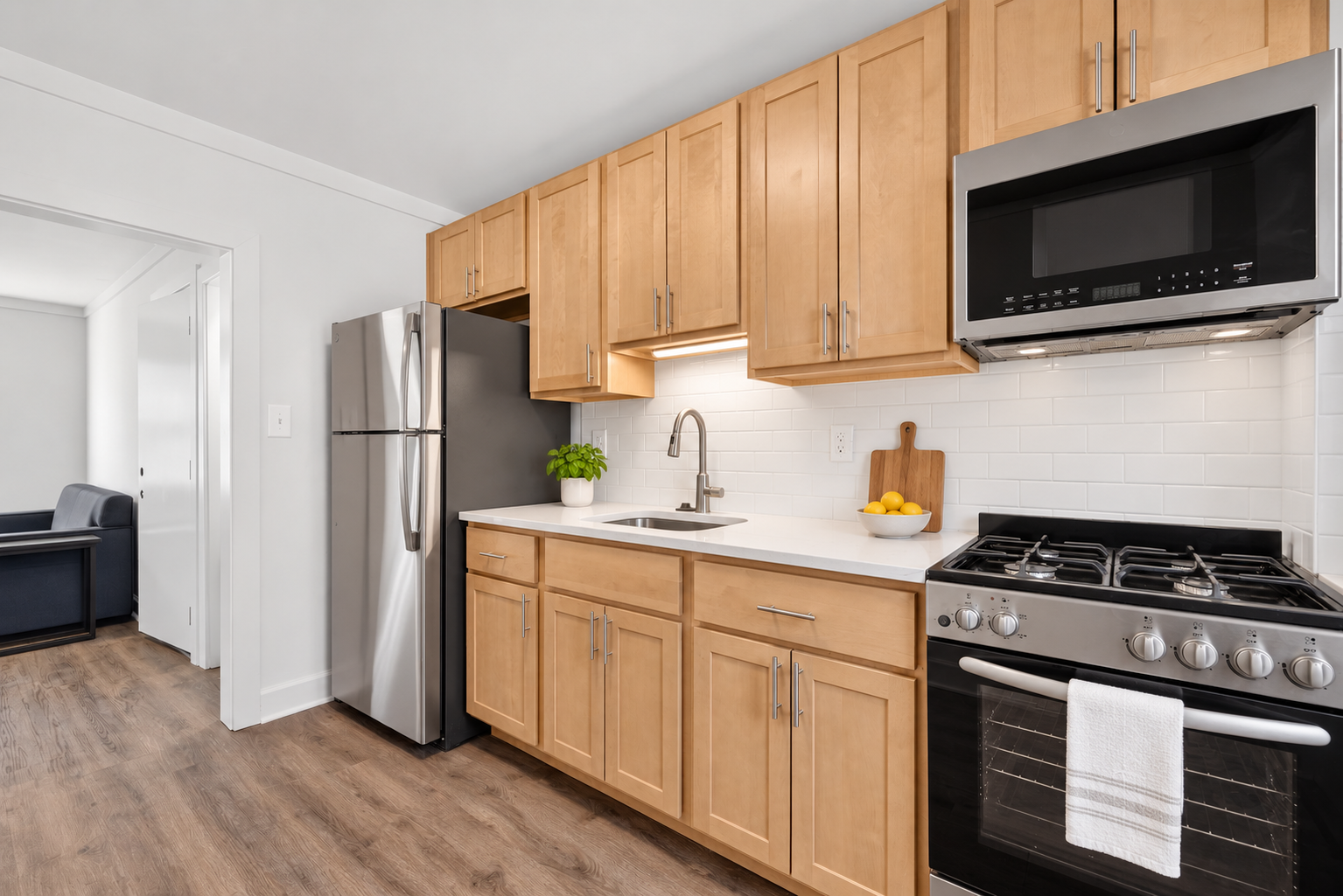 The Welcome Inn's fully-equipped kitchen with wooden cabinets, stainless steel refrigerator, black microwave, stainless steel stove, white countertop, and white subway tile backsplash.