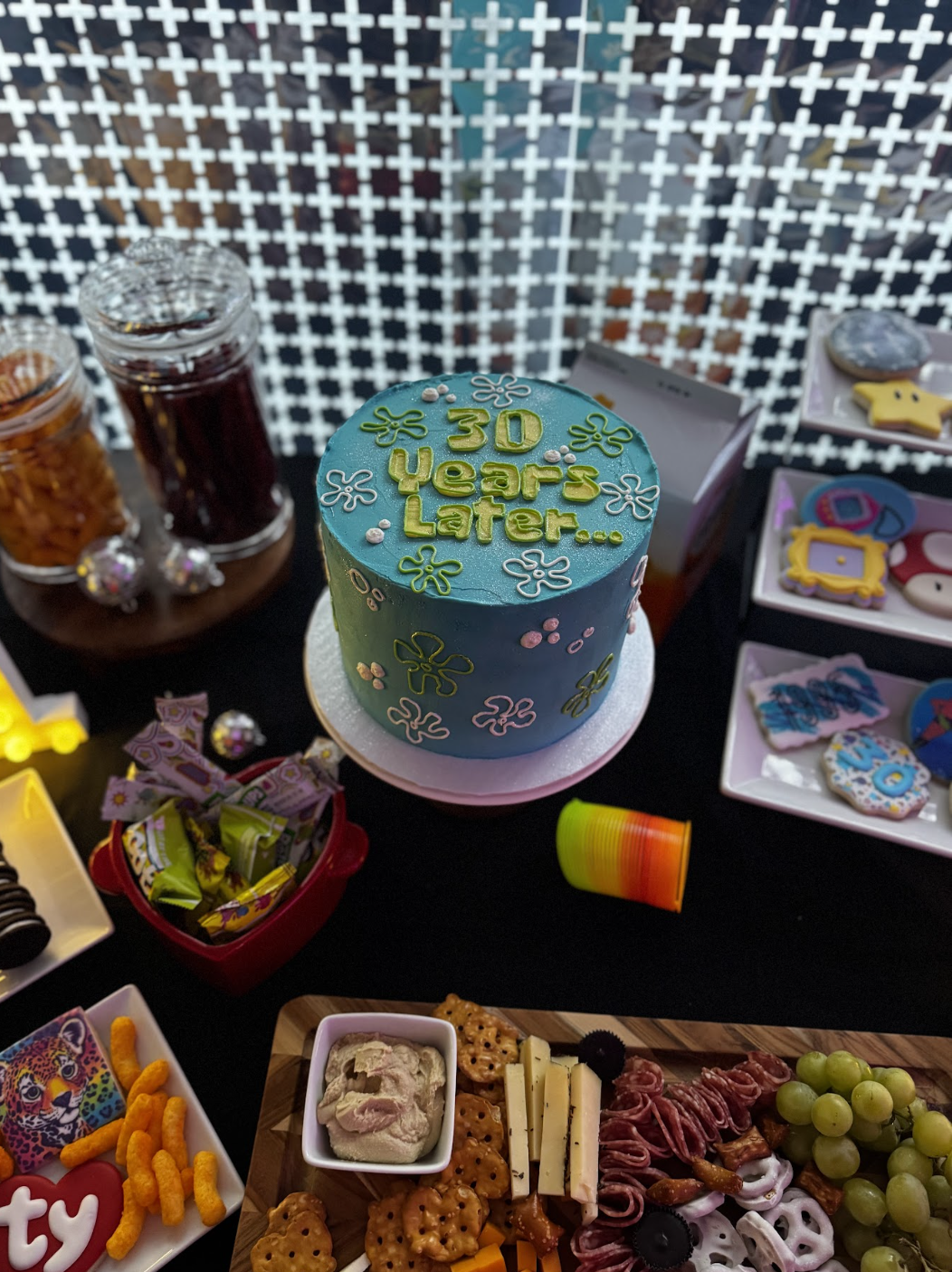 A birthday celebration table featuring a blue cake with the message "30 Years Later...", assorted snacks, candies, and decorated cookies.