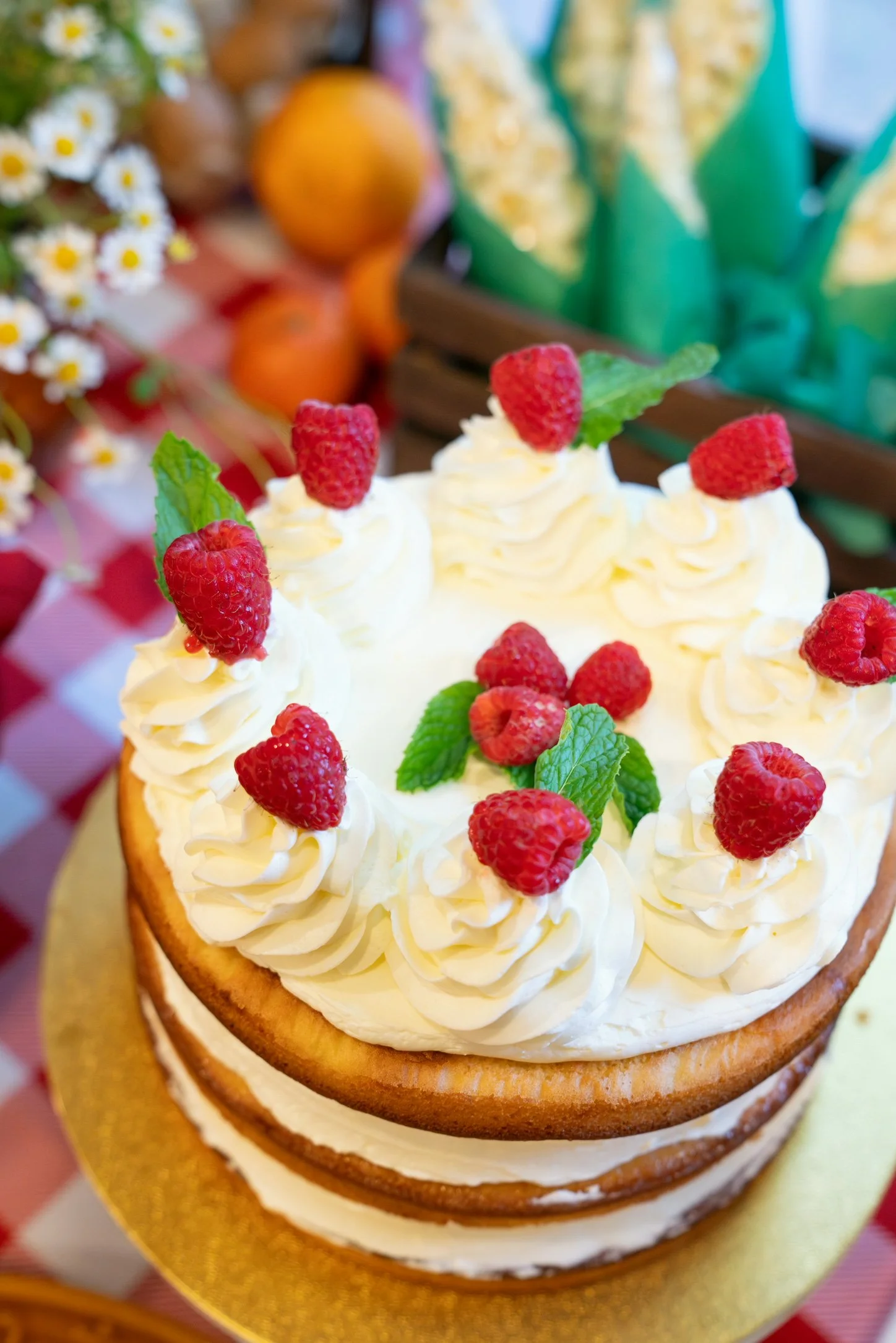 A close-up of a layered cake decorated with white frosting, fresh raspberries, and mint leaves.