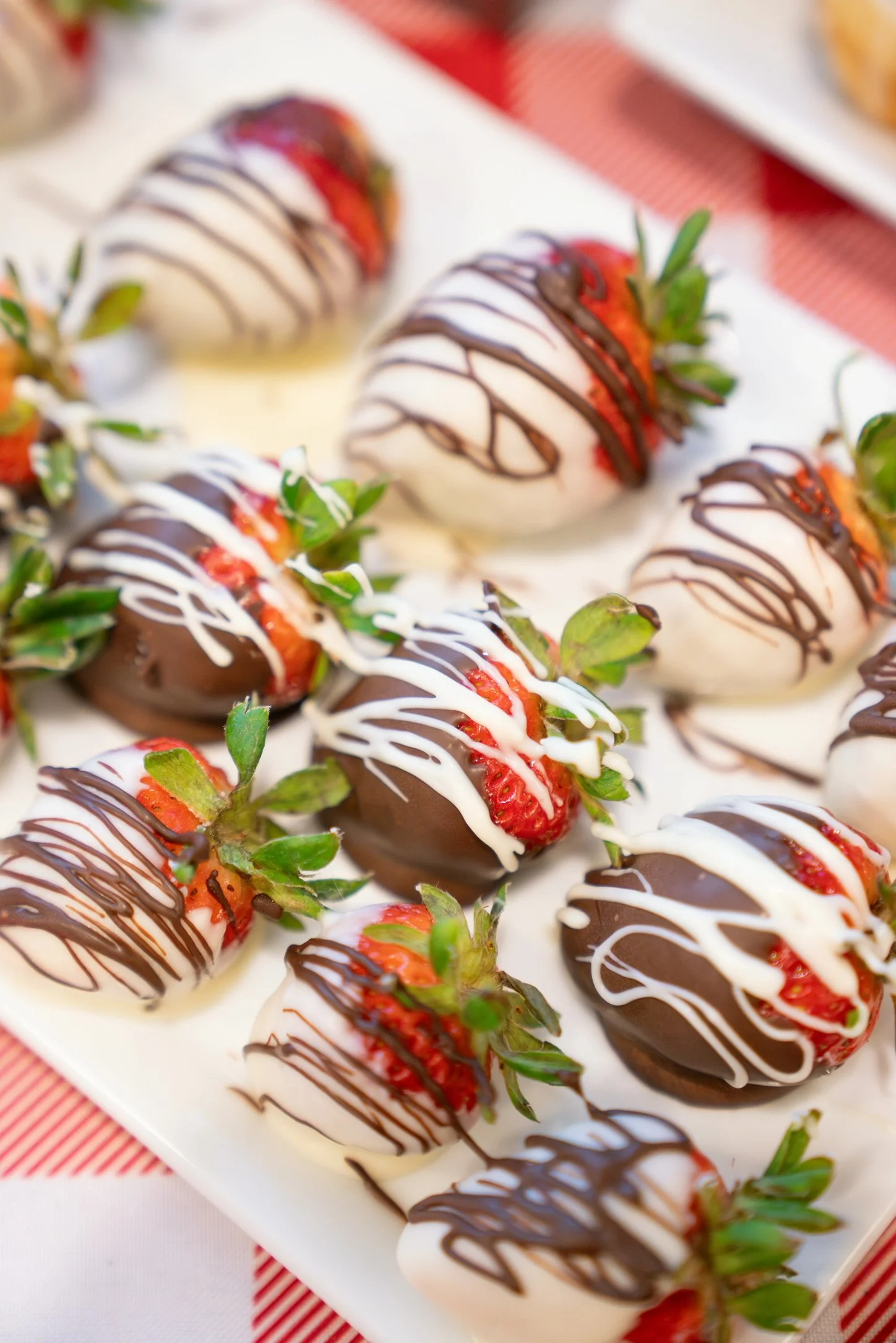 Strawberries dipped in white and dark chocolate with drizzles, arranged on a white plate.