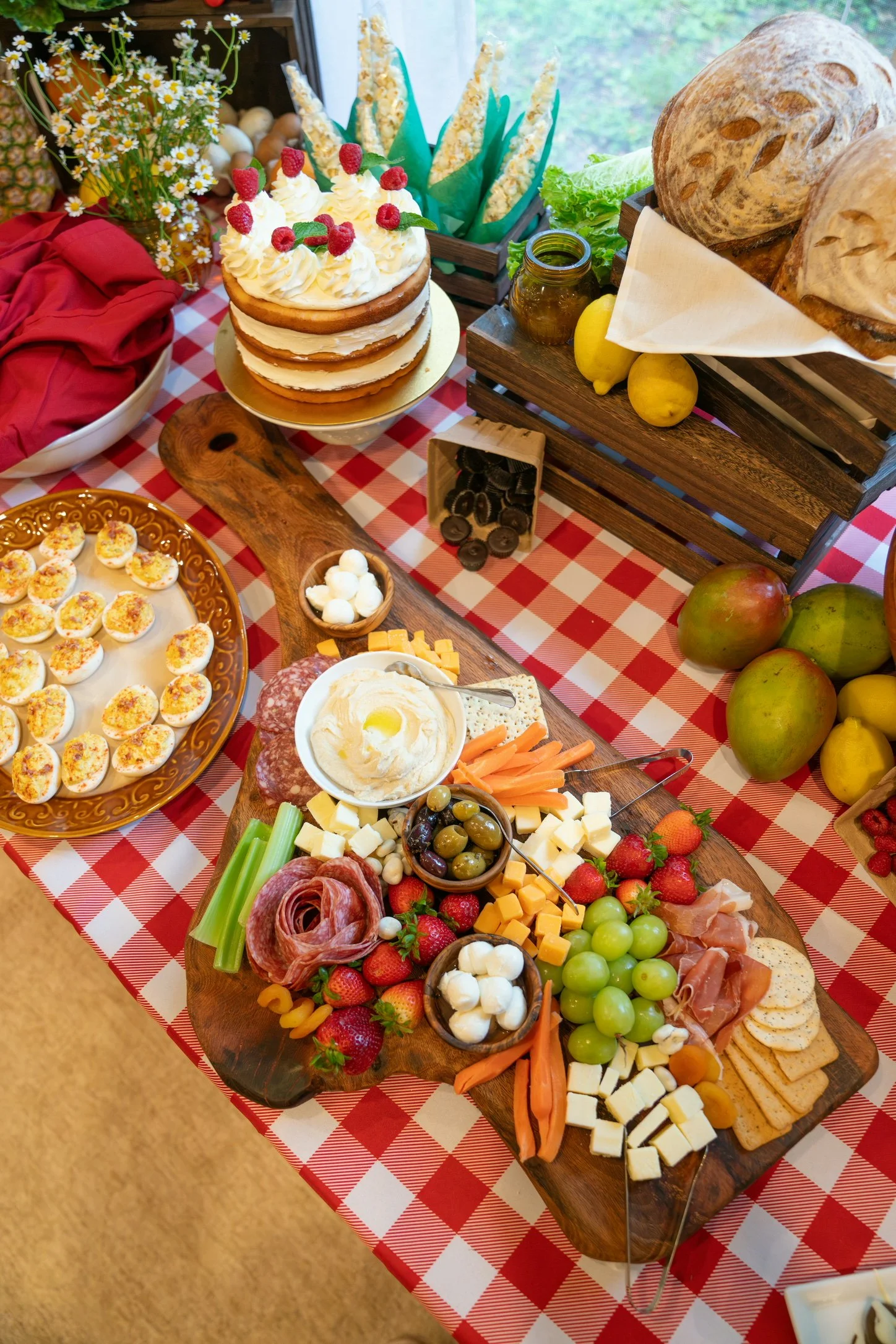A cheese and charcuterie board with assorted cheeses, cured meats, grapes, strawberries, vegetables, and olives, on a wooden platter.