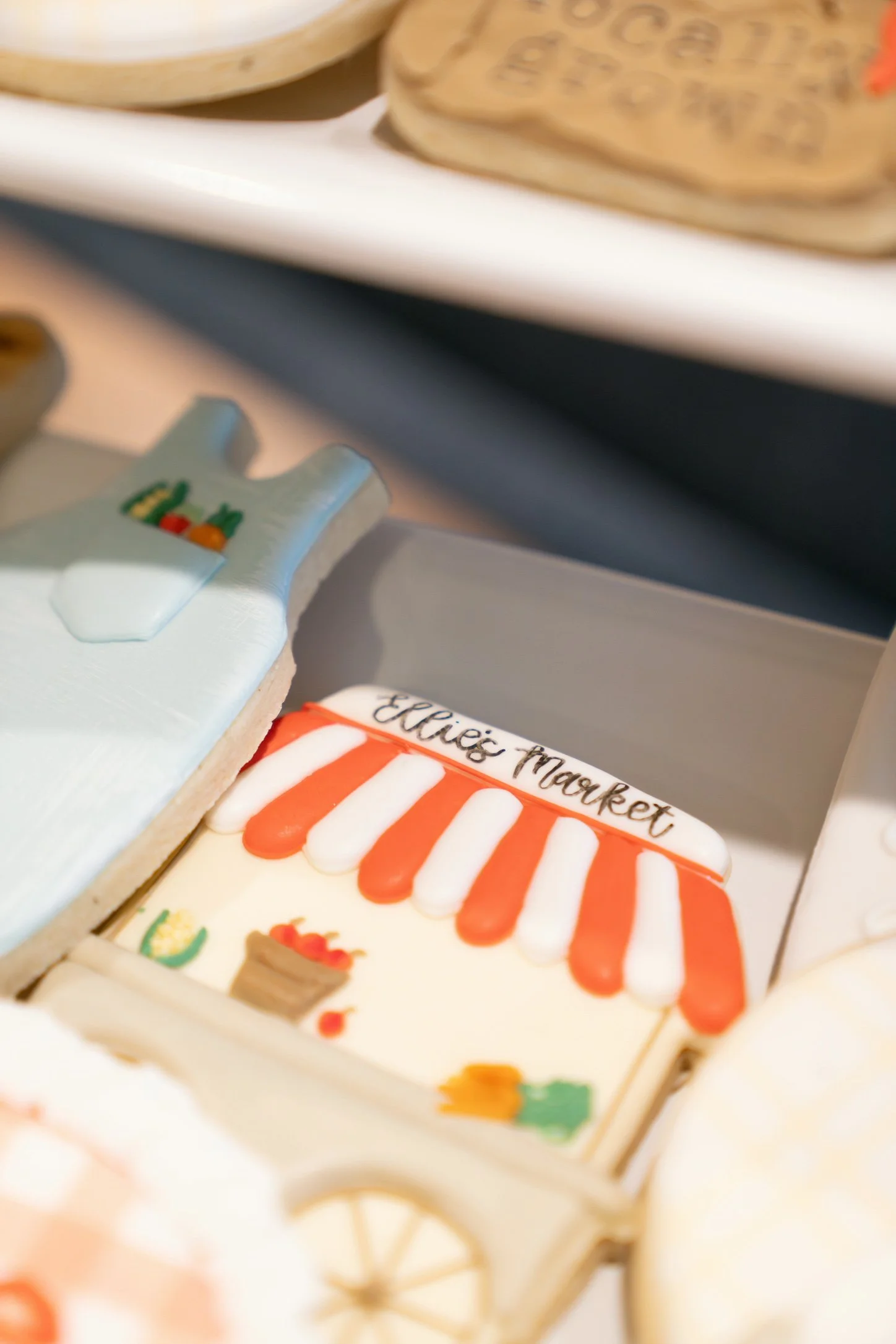 Decorated cookies with festive designs, one featuring the text 'Elic's Market' and colorful icing, arranged on a white tray.