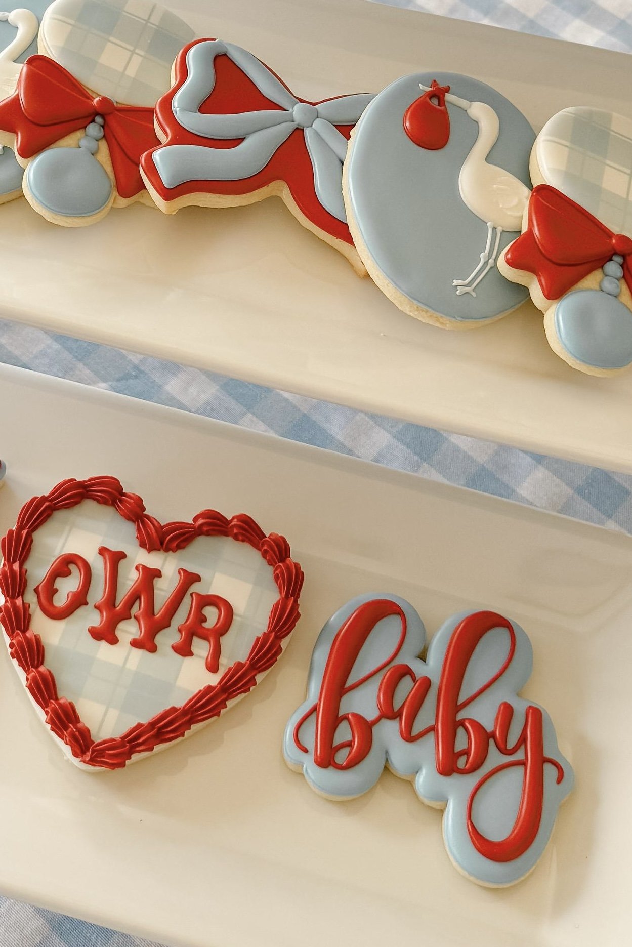 Decorative cookies for a baby shower, including a heart-shaped cookie with red and white icing that reads 'WATER' and a sign that says 'Baby' with red icing.